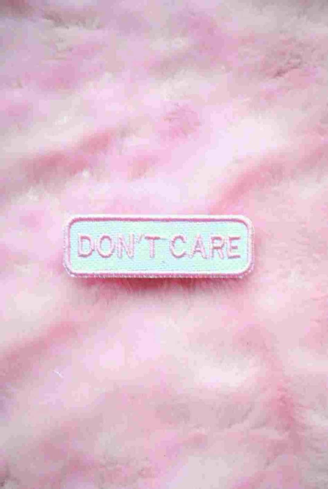 桌布 壁紙 — 一個長方形刺繡補丁，上面有「DON'T CARE」字樣，放在柔軟的粉紅色毛絨表面上。