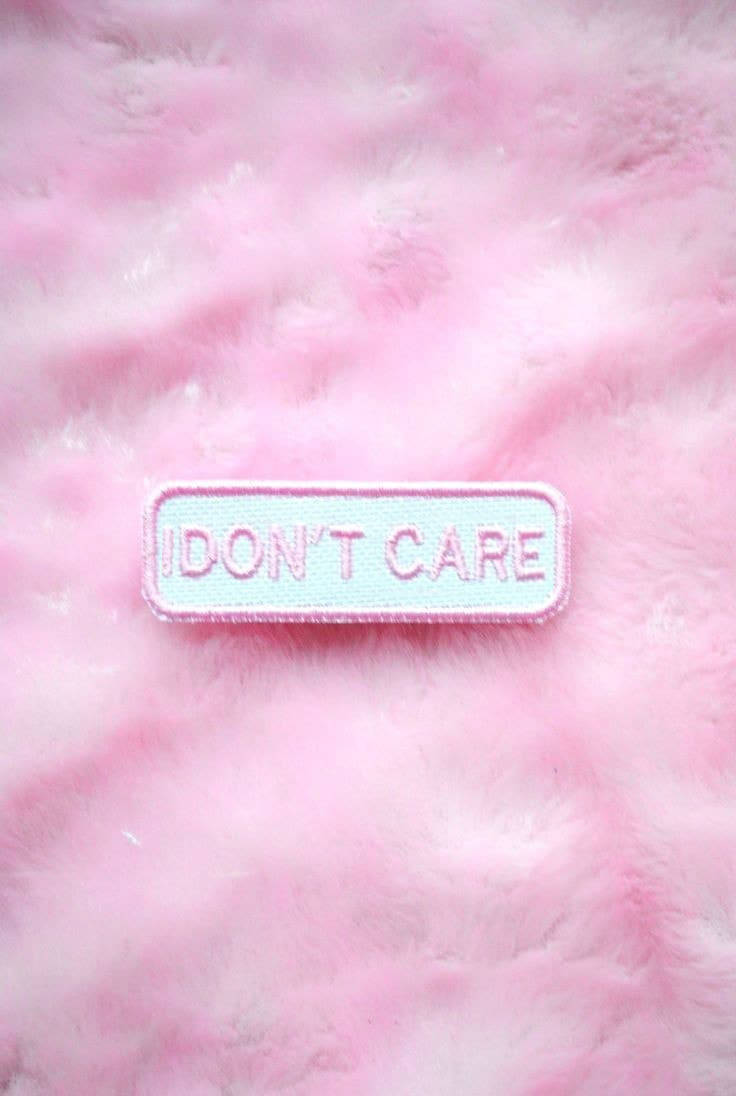 I Dont Care 桌布 壁紙 — 一個長方形的補丁，上面寫著 'I DON'T CARE'，放在柔軟毛茸茸的粉紅色布料背景上。