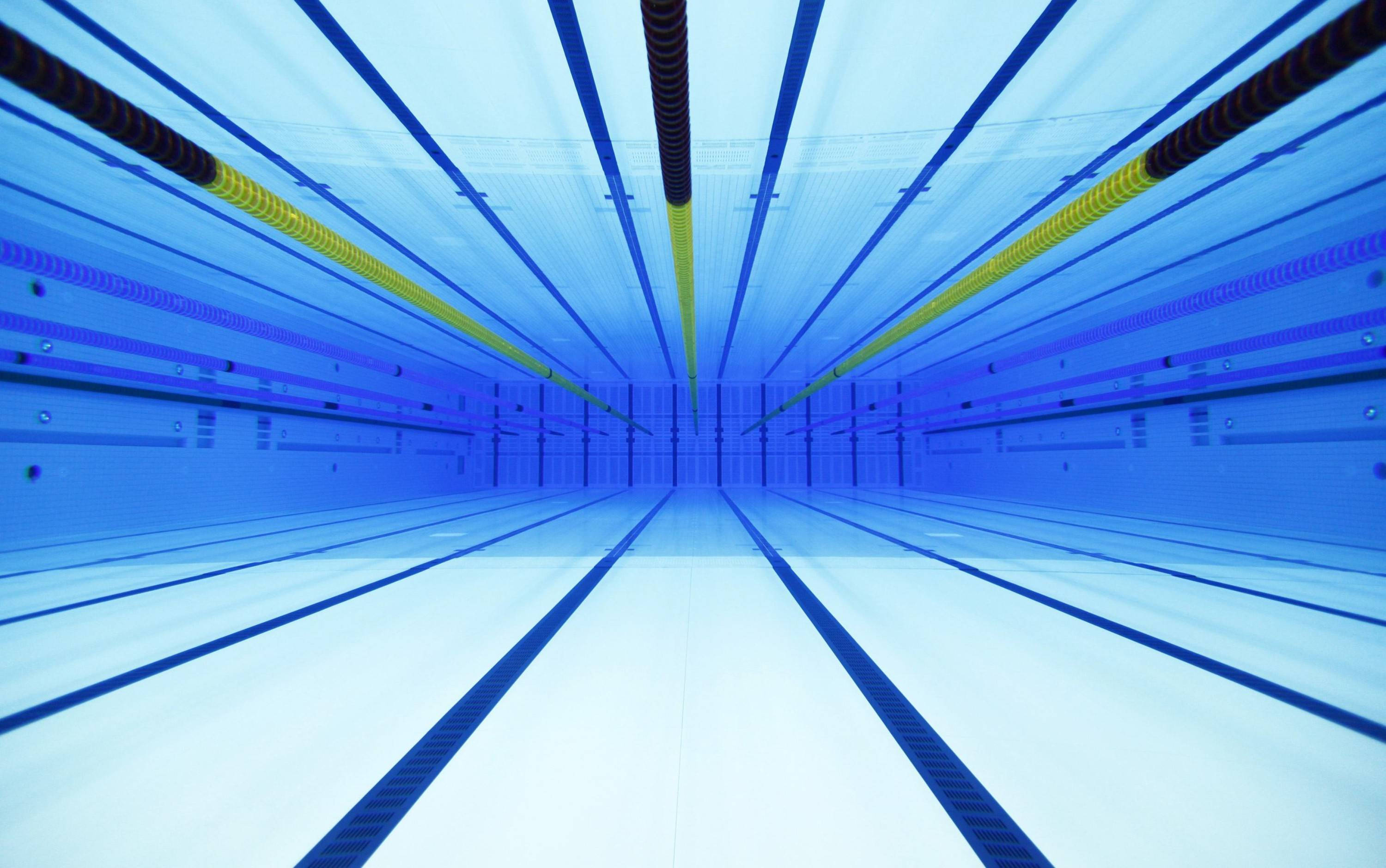 Swimming 桌布 壁紙 — 一個長而空的游泳池，藍色的水和黃色的泳道分隔線向遠方延伸。