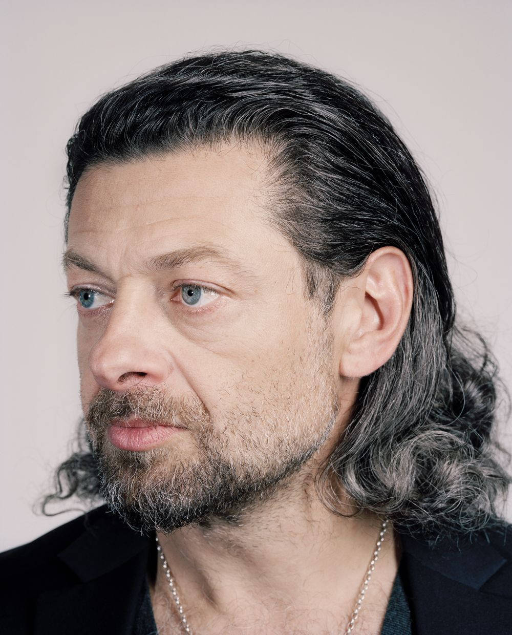 actor 桌布 壁紙 — 一個長著深色長髮和灰色條紋的男人，在純色背景前若有所思地側視的特寫肖像。