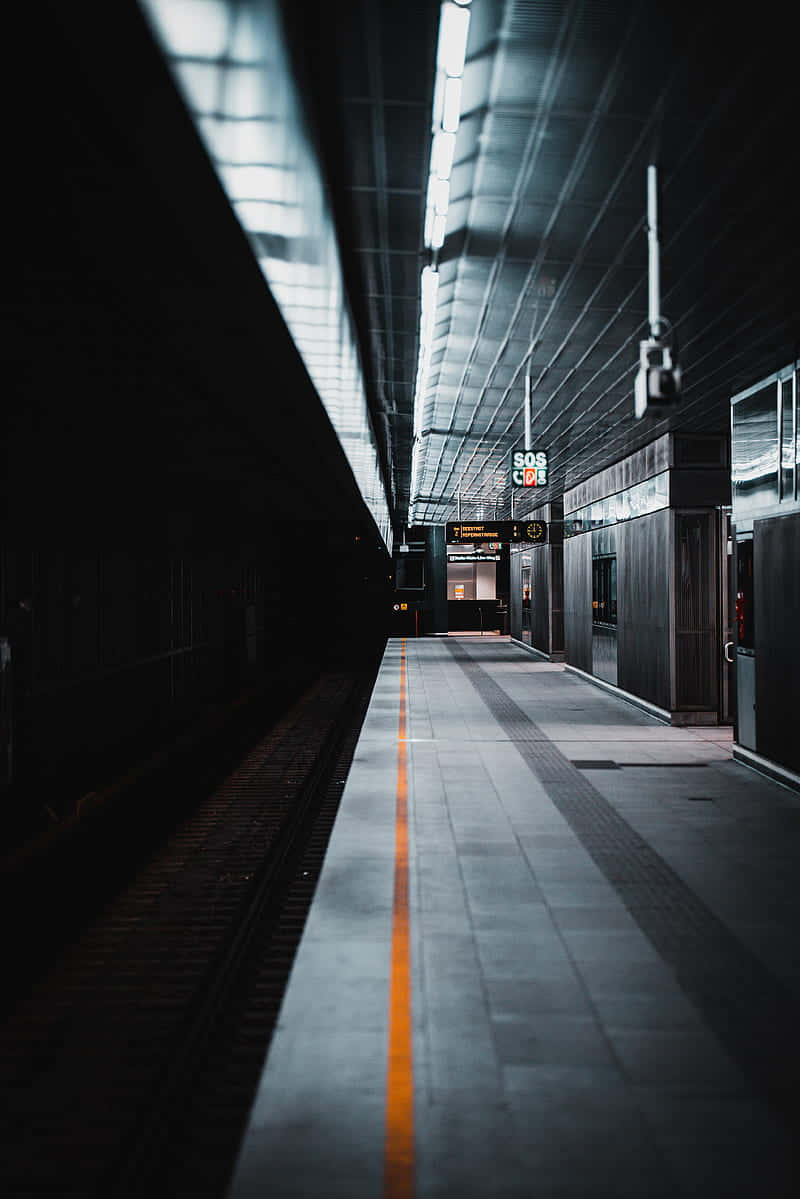 Metro 桌布 壁紙 — 一個長長的空蕩地鐵月台，沐浴在刺眼的螢光燈下，中央有一條醒目的橙色安全線。