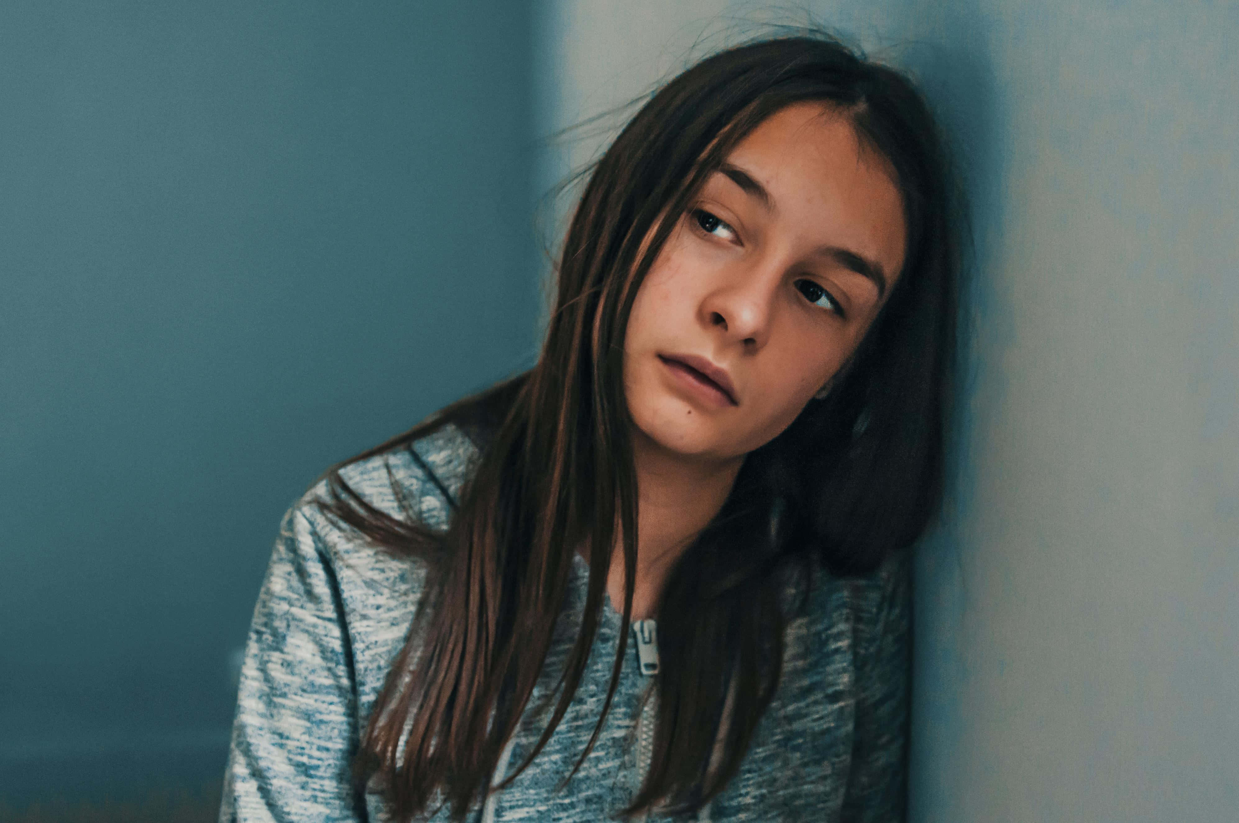 Depressed 桌布 壁紙 — 一個長長黑髮的年輕女孩靠著冰冷的藍色牆壁，她疲倦的目光和微微張開的嘴唇傳達出靜靜的憂鬱。