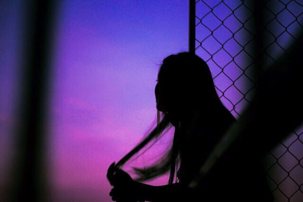 Woman 桌布 壁紙 — 一個長髮人物的剪影，站在鐵絲網圍欄後面，背景是充滿活力的紫色和粉紅色黃昏天空。