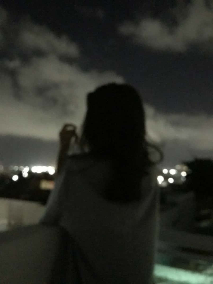 女孩 桌布 壁紙 — 一個長髮人物的模糊剪影夜晚站在屋頂上，凝視著被遠處燈光照亮的城市景觀。