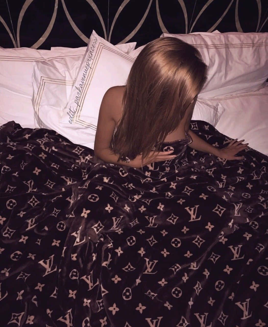 Boujee Aesthetic 桌布 壁紙 — 一個長髮的人坐在床上，床上鋪著帶有重複字母組合圖案的深色天鵝絨毯子。
