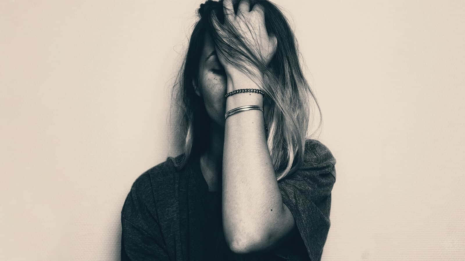 Depressed 桌布 壁紙 — 一個長髮的人用一隻手遮住臉，靠著素色牆壁，呈現單色調。