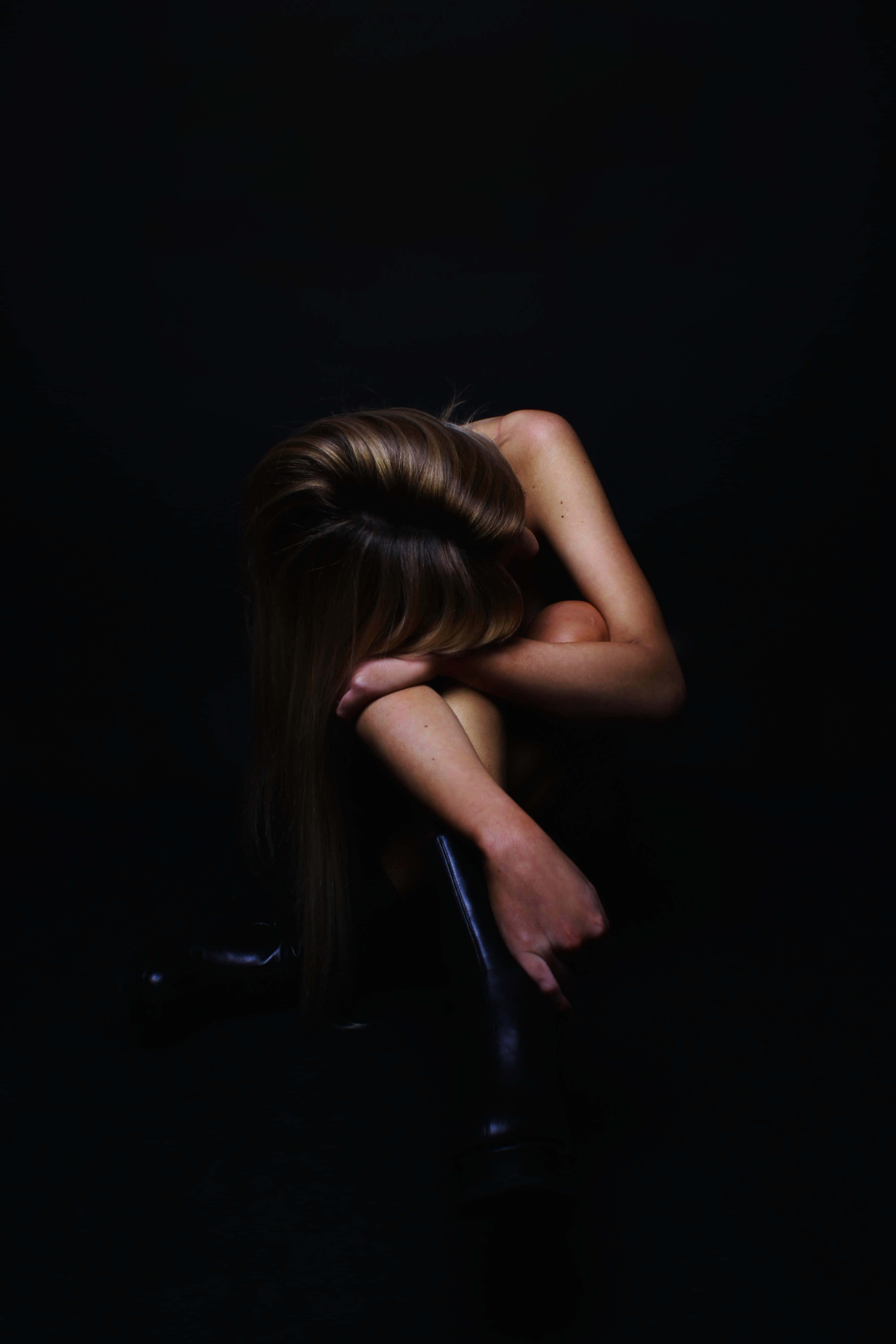 Depression Girl 桌布 壁紙 — 一個長髮的人蜷縮成一個緊密的球體，背景漆黑，雙臂環抱膝蓋，姿態充滿深深的孤獨。