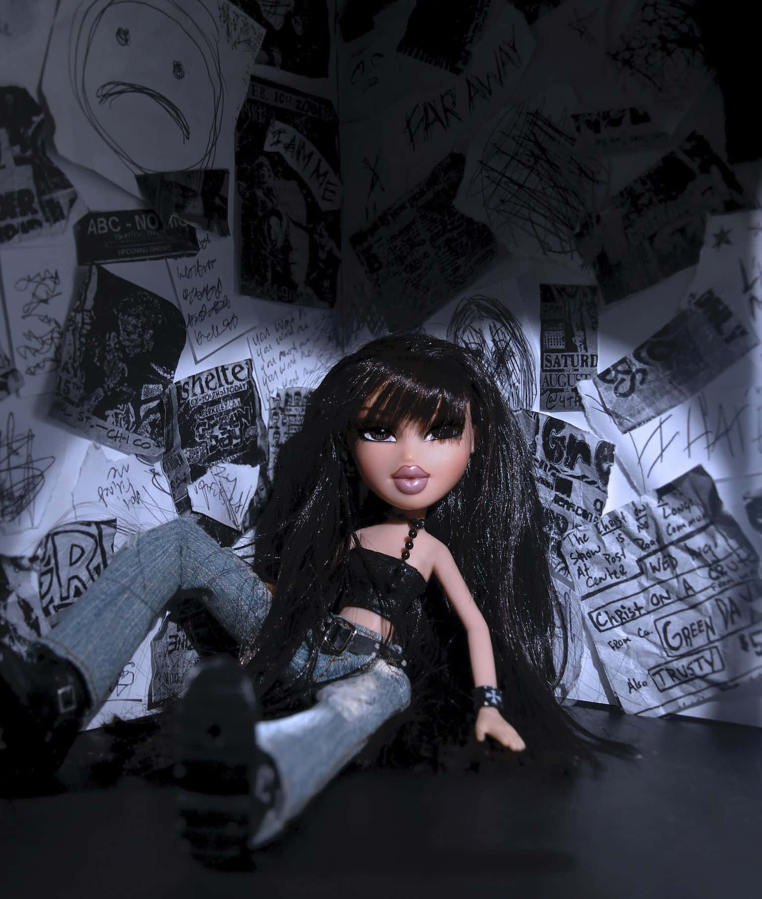 bratz 美學 桌布 壁紙 — 一個長黑髮、穿著龐克服飾的洋娃娃坐在昏暗的空間中，周圍環繞著混亂的手寫筆記和圖畫。