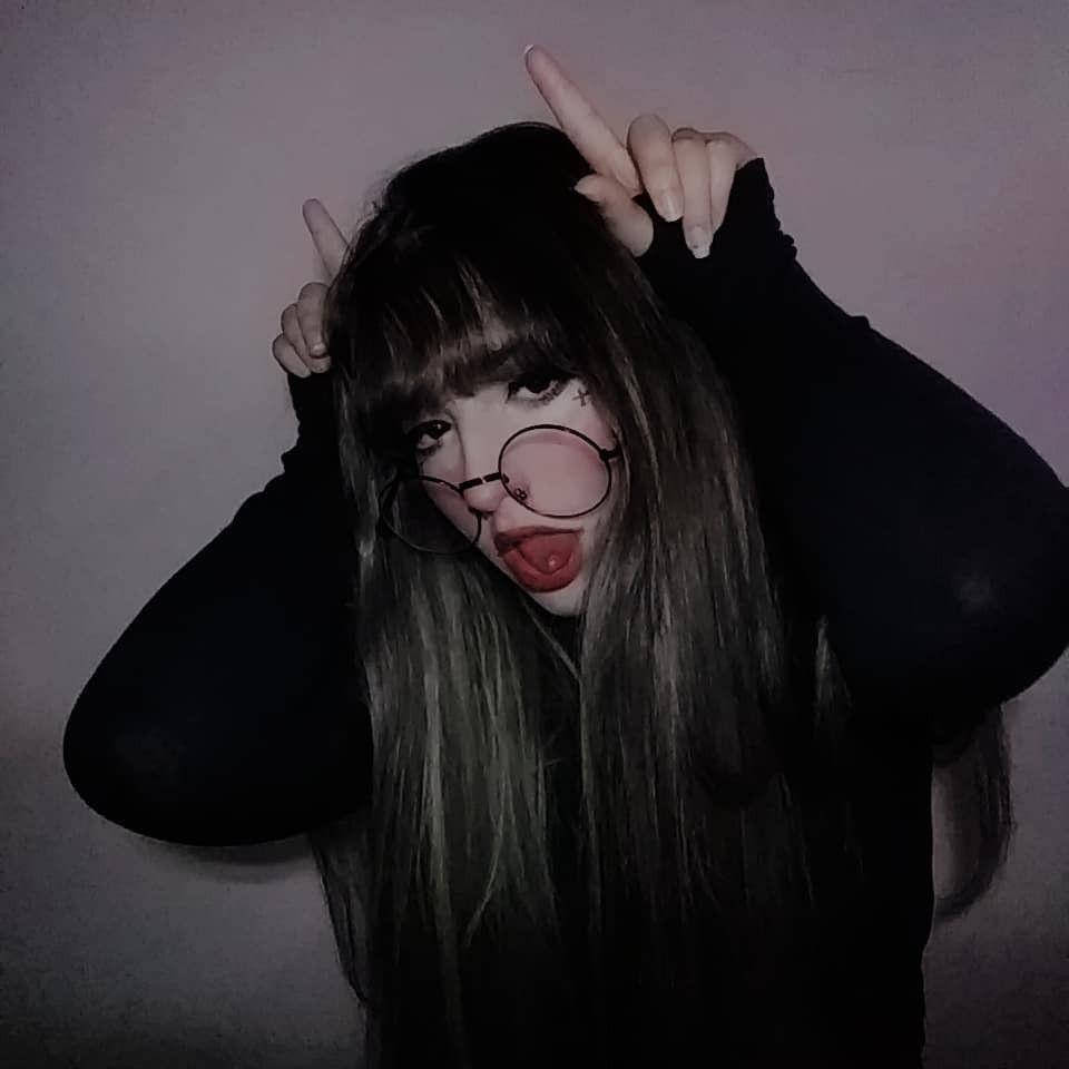 垃圾美學 桌布 壁紙 — 一個長黑髮戴眼鏡的人，對著素牆做出鬼臉，同時舉起魔鬼角。