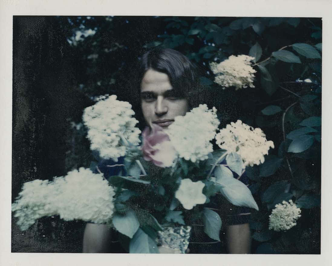 andy warhol 桌布 壁紙 — 一個長黑髮的人拿著一束白色繡球花和一朵粉紅玫瑰，背景是深色樹葉。