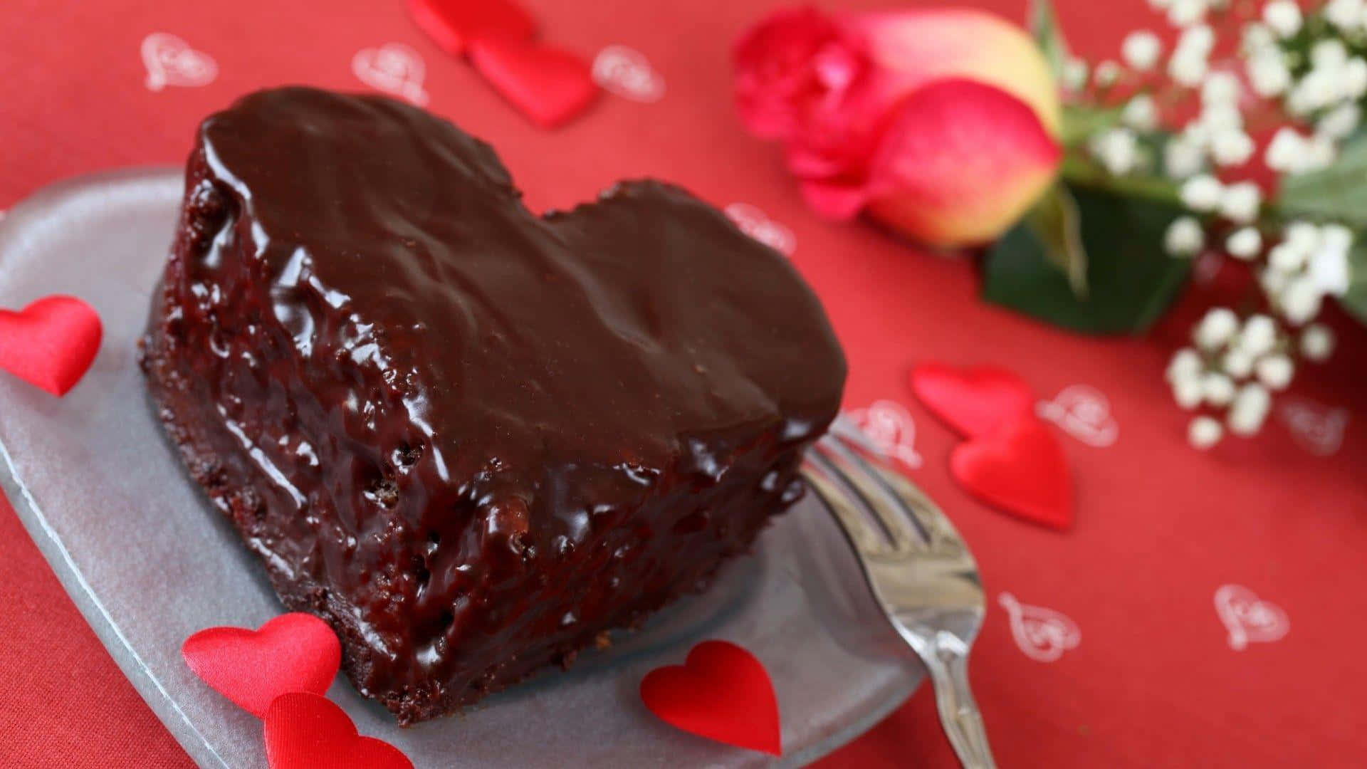 Chocolate Cake 桌布 壁紙 — 一個閃亮的巧克力心形蛋糕放在銀盤上，周圍有紅心和玫瑰，放在紅色桌布上。