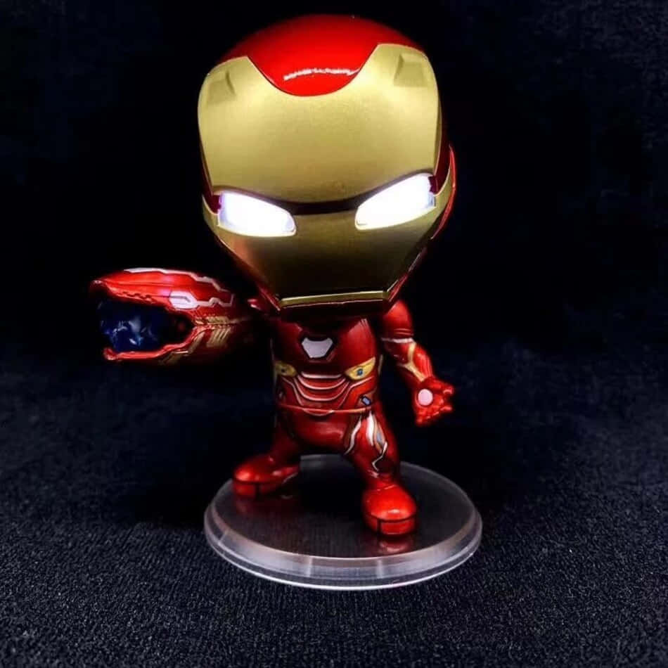 Iron Man Bobbleheads 桌布 壁紙 — 一個閃亮的紅色和金色鋼鐵人人偶站在透明底座上，手持無限手套，背景為深色紋理。