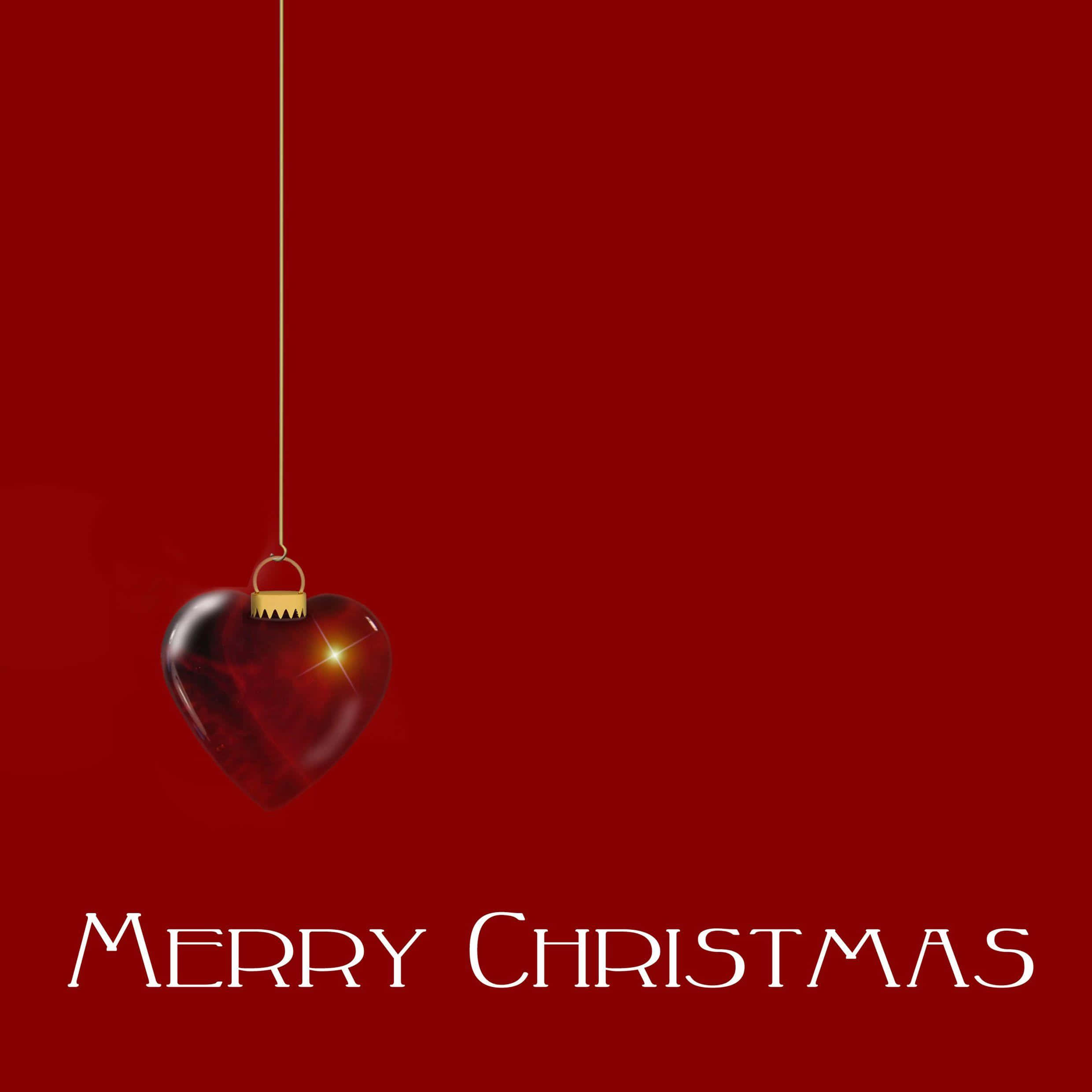 Christmas Card 桌布 壁紙 — 一個閃亮的紅色心形裝飾品用金色繩子掛在純紅色背景上，下方有「聖誕快樂」文字。