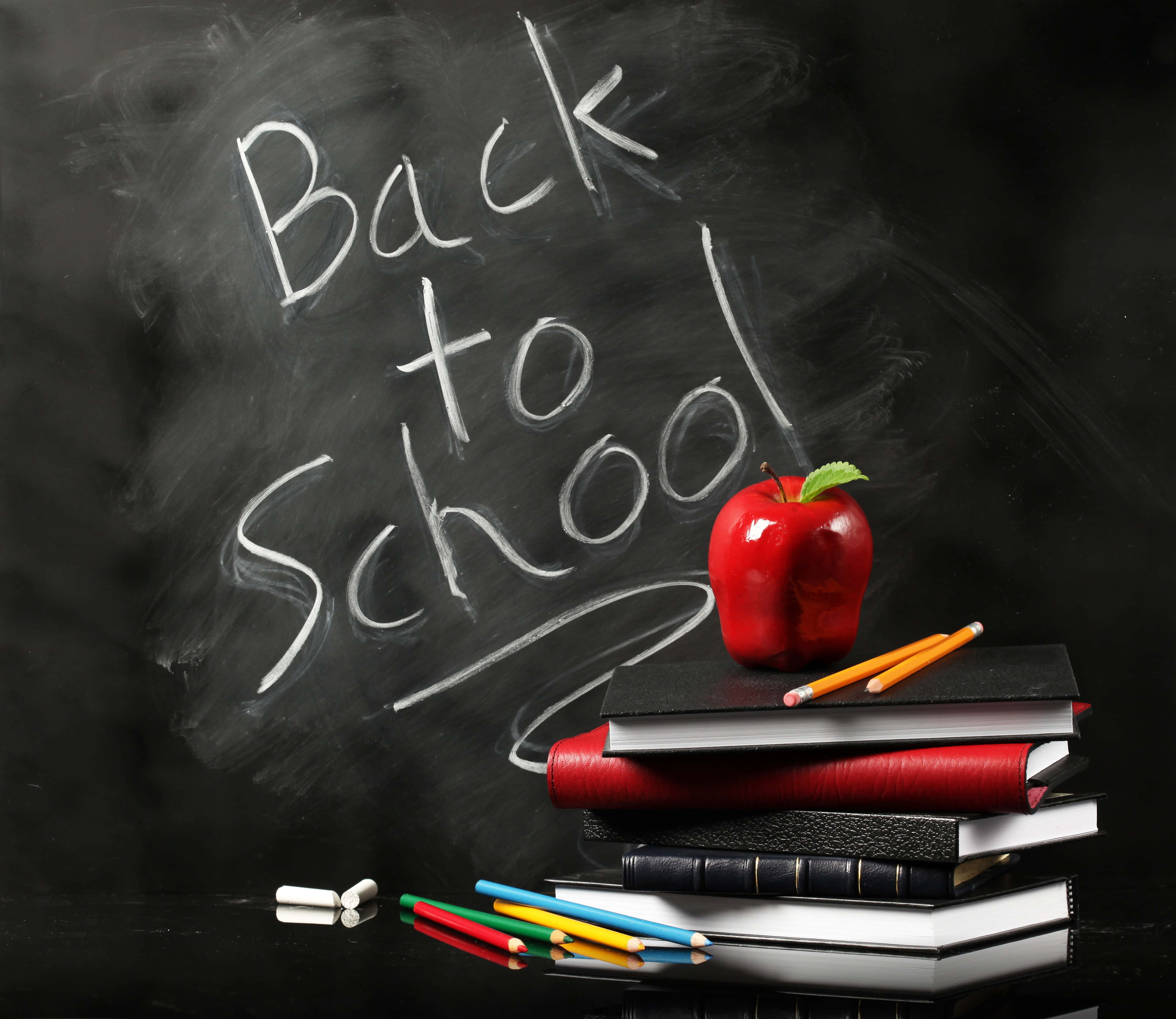 Back To School 桌布 壁紙 — 一個閃亮的紅蘋果放在一堆色彩繽紛的書本上，旁邊是深色黑板上用粉筆畫的「Back to School」。