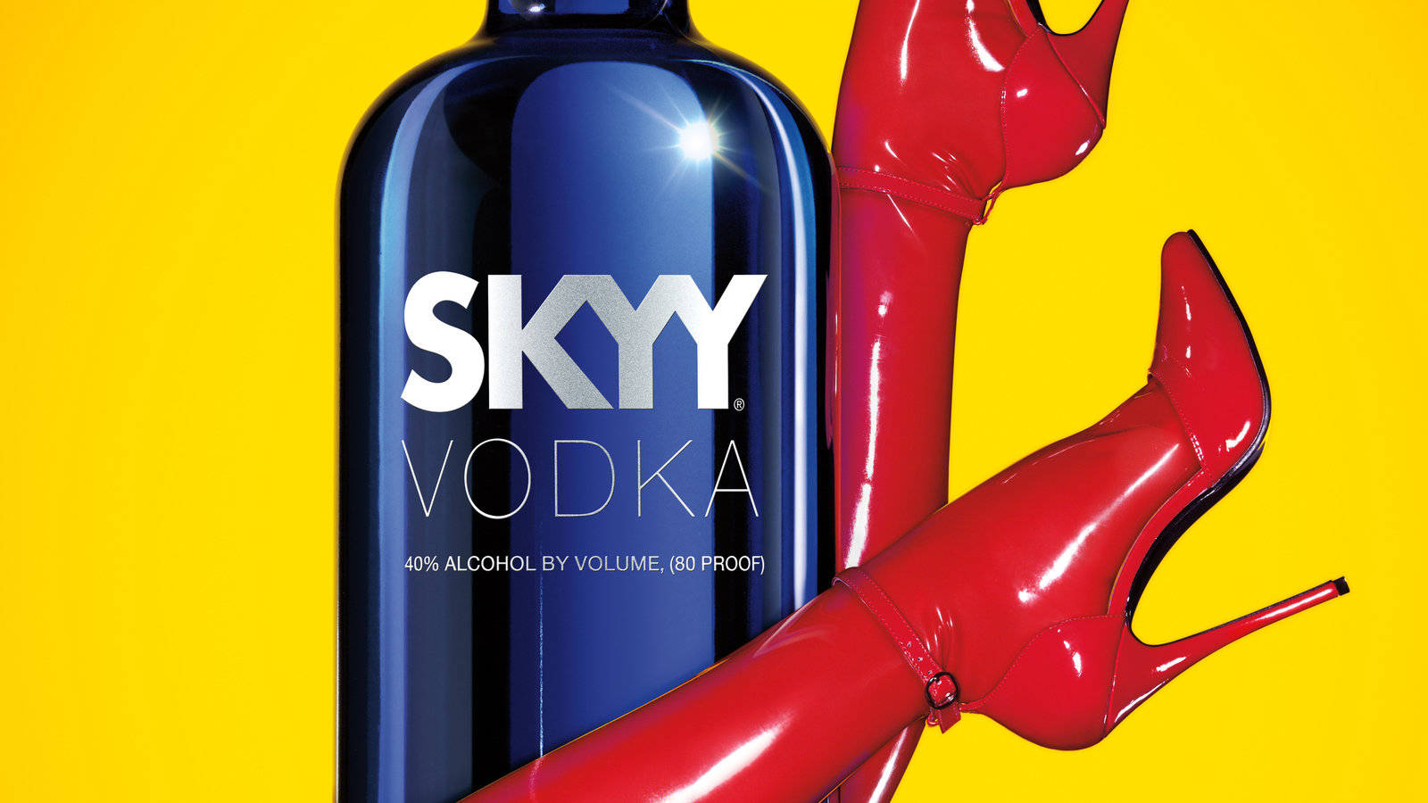 Drink 桌布 壁紙 — 一個閃亮的藍色Skyy伏特加酒瓶旁邊有一對閃亮的紅色高跟鞋，背景是鮮黃色。