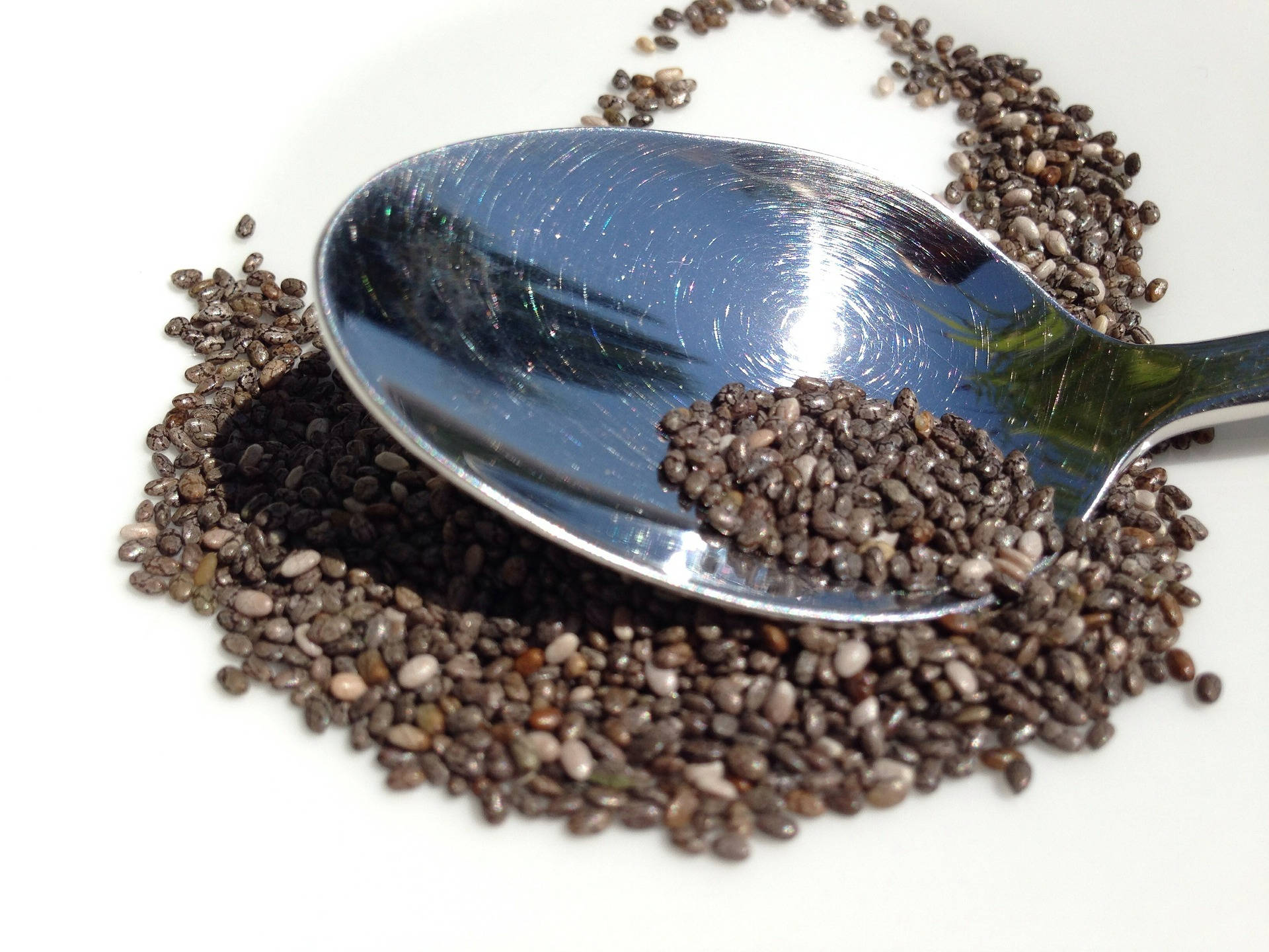 Healthy Food 桌布 壁紙 — 一個閃亮的金屬湯匙將深色斑點的奇亞籽以優雅的弧線灑落在潔白的表面上。