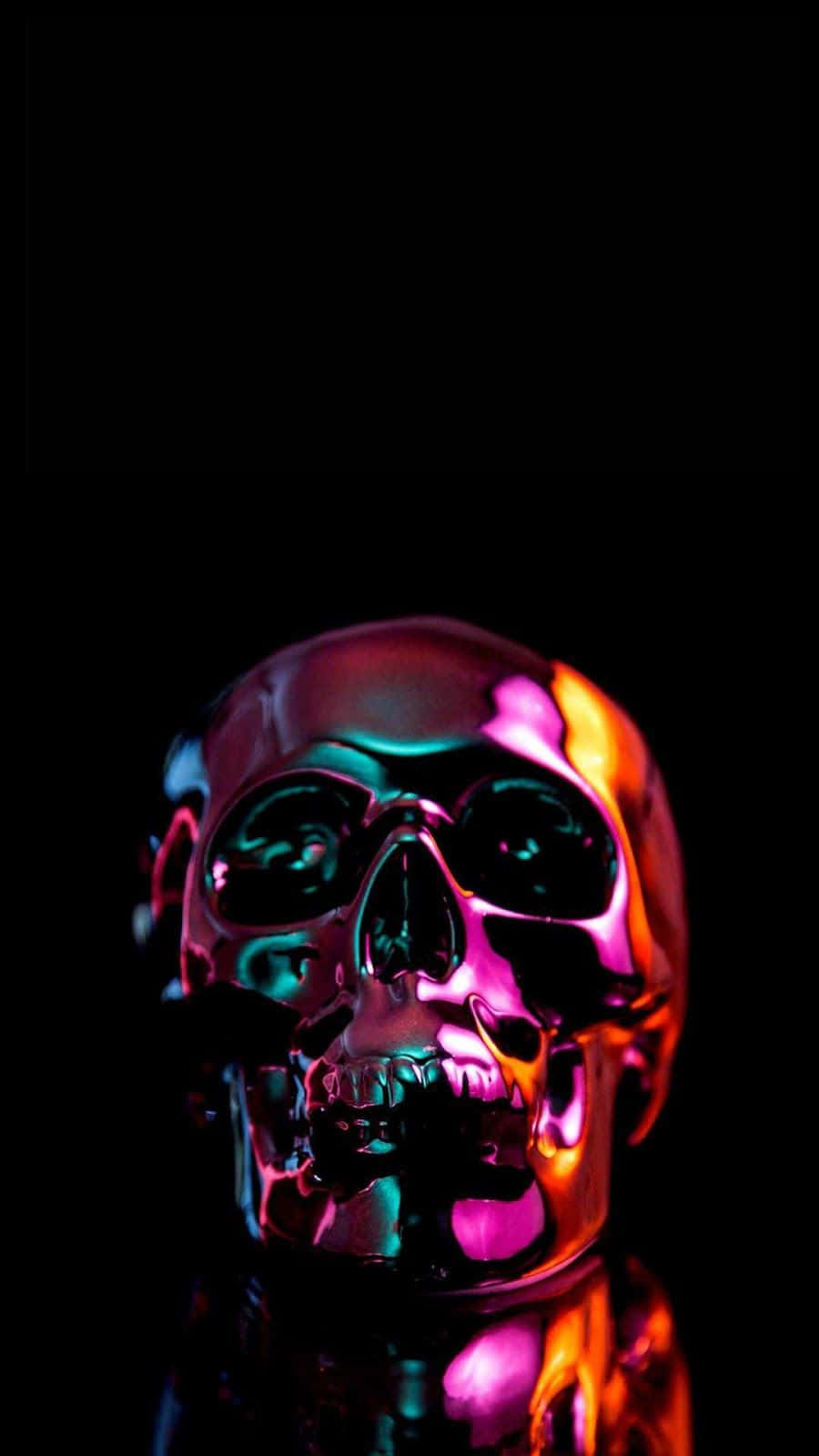 Aesthetic iPhone Horror 桌布 壁紙 — 一個閃亮的金屬骷髏頭在純黑色背景上反射出霓虹粉紅和青色燈光。