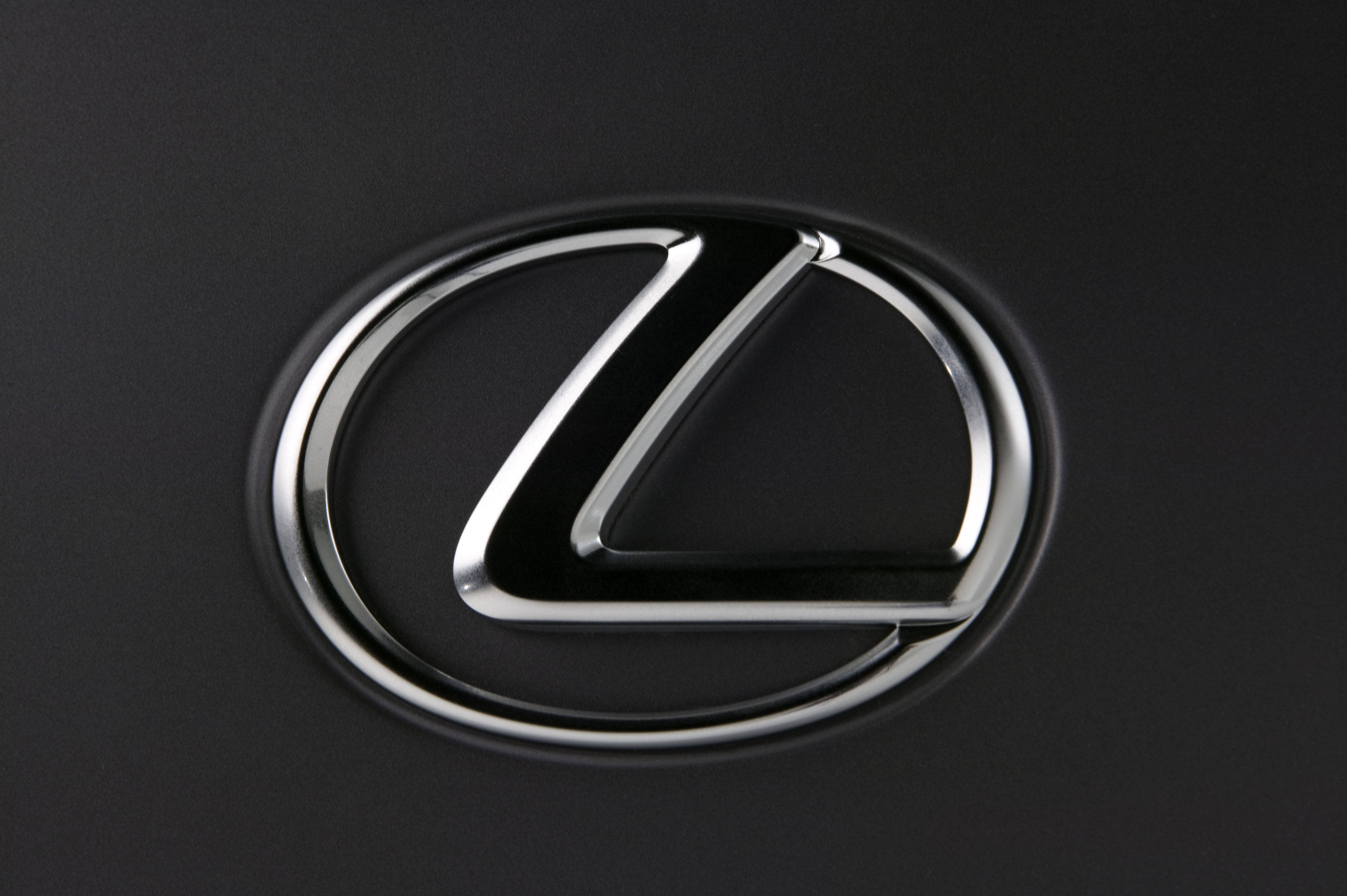 lexus logo 桌布 壁紙 — 一個閃亮的鉻色凌志標誌特寫，映襯在霧面黑色汽車表面上。