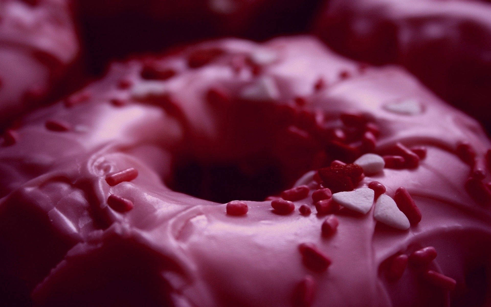 Donut 桌布 壁紙 — 一個閃亮粉紅色糖霜甜甜圈的近距離特寫，上面有紅色和白色心形糖粒。