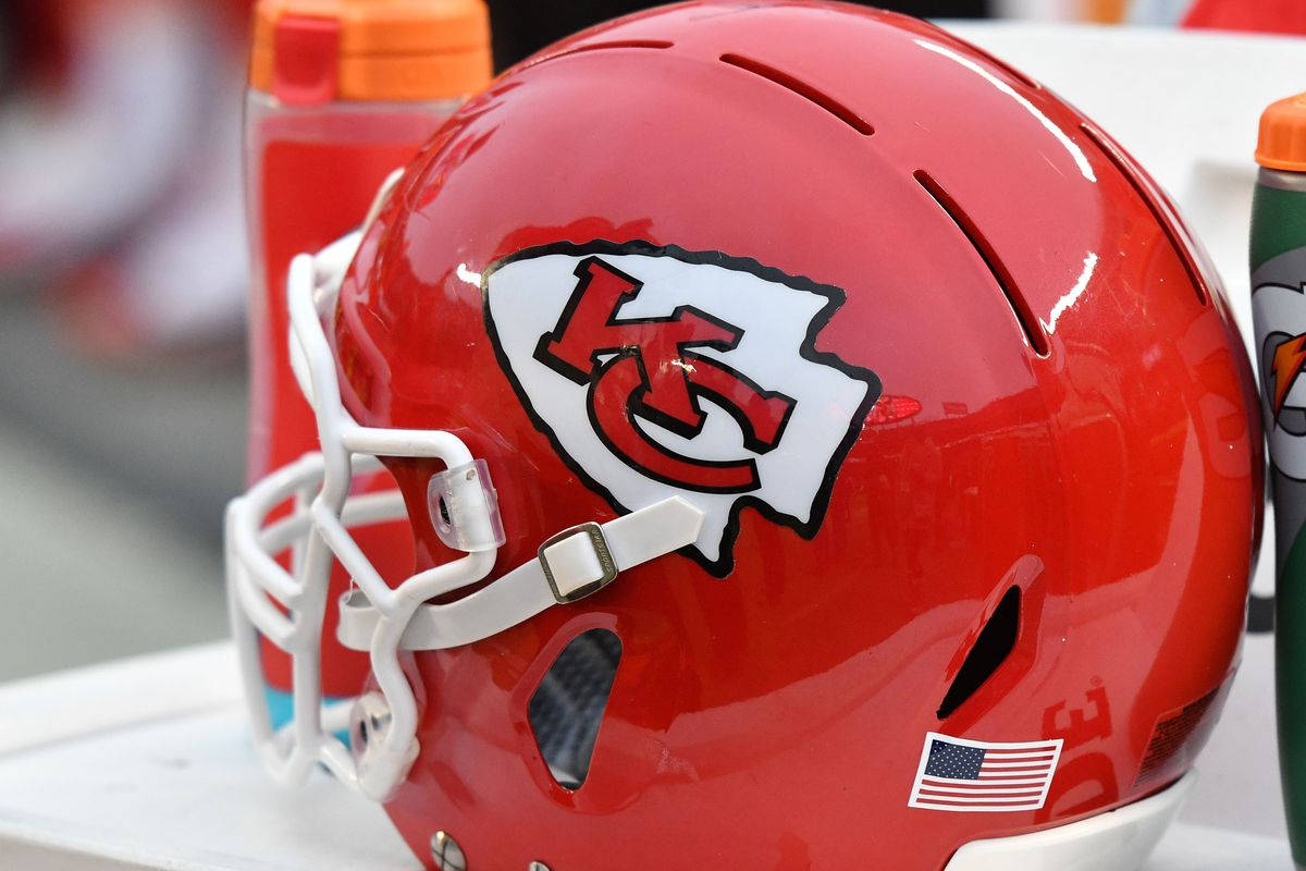 Kansas City Chiefs Logo 桌布 壁紙 — 一個閃亮紅色堪薩斯城酋長隊美式足球頭盔的特寫，帶有白色面罩和美國國旗貼紙。