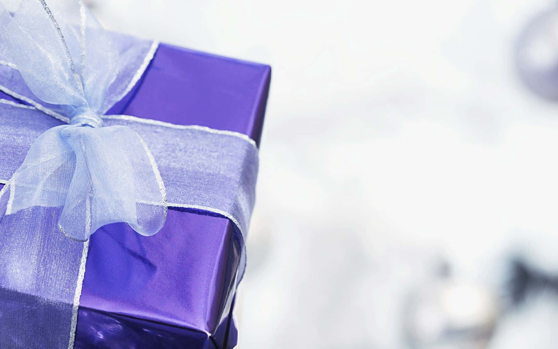 Gift 桌布 壁紙 — 一個閃亮紫色禮物盒的特寫，繫著精緻的淺藍色絲帶蝴蝶結，背景是柔和的白色。
