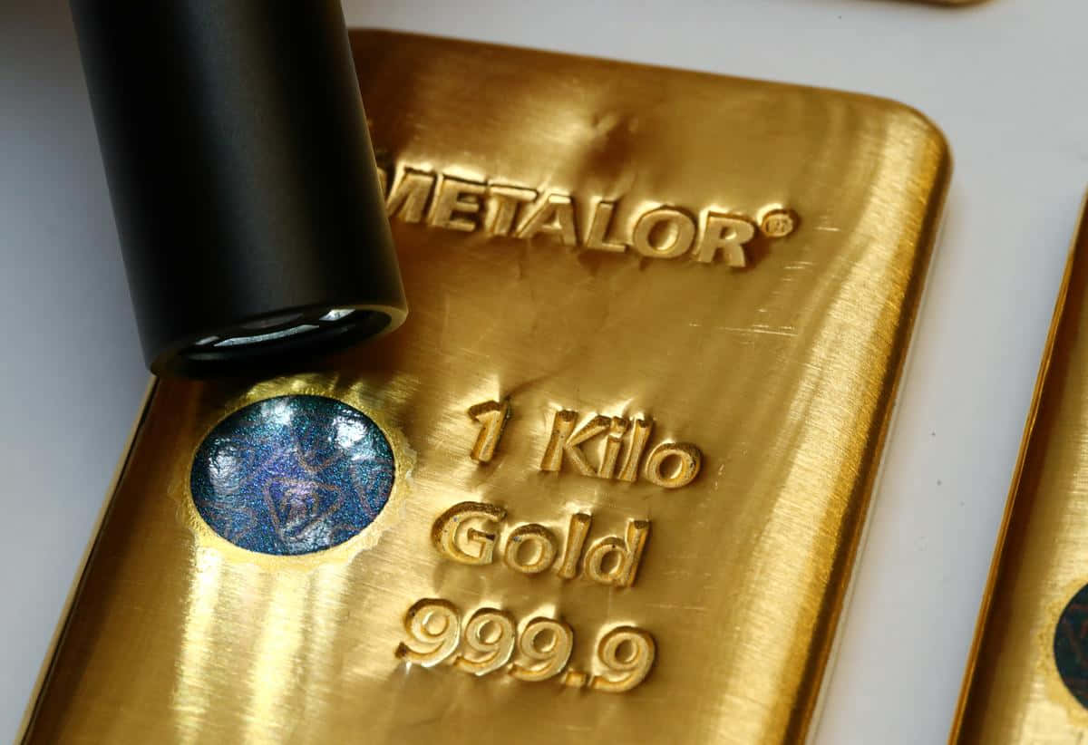 Gold Bar 桌布 壁紙 — 一個閃亮金條的特寫，標有「1 Kilo Gold 999.9」，帶有藍色全息封條和附近的黑色印章。