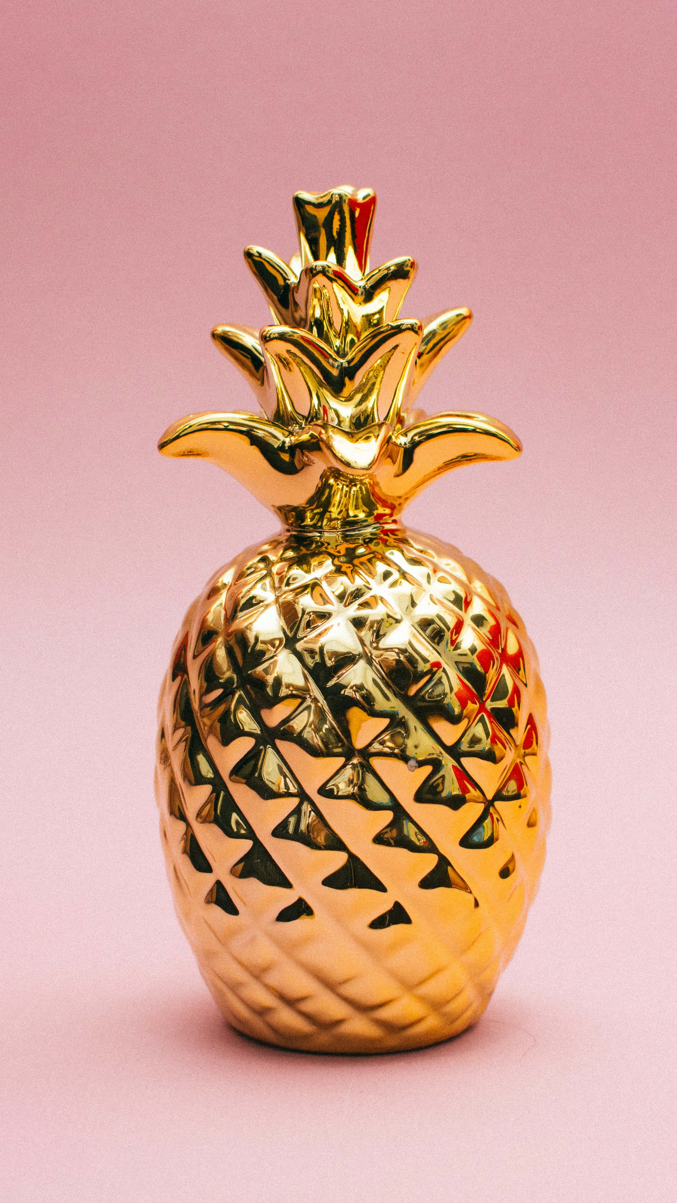 Pineapple 桌布 壁紙 — 一個閃亮金色鳳梨擺設，帶有細緻紋理的果皮，立於柔和粉紅色背景前。