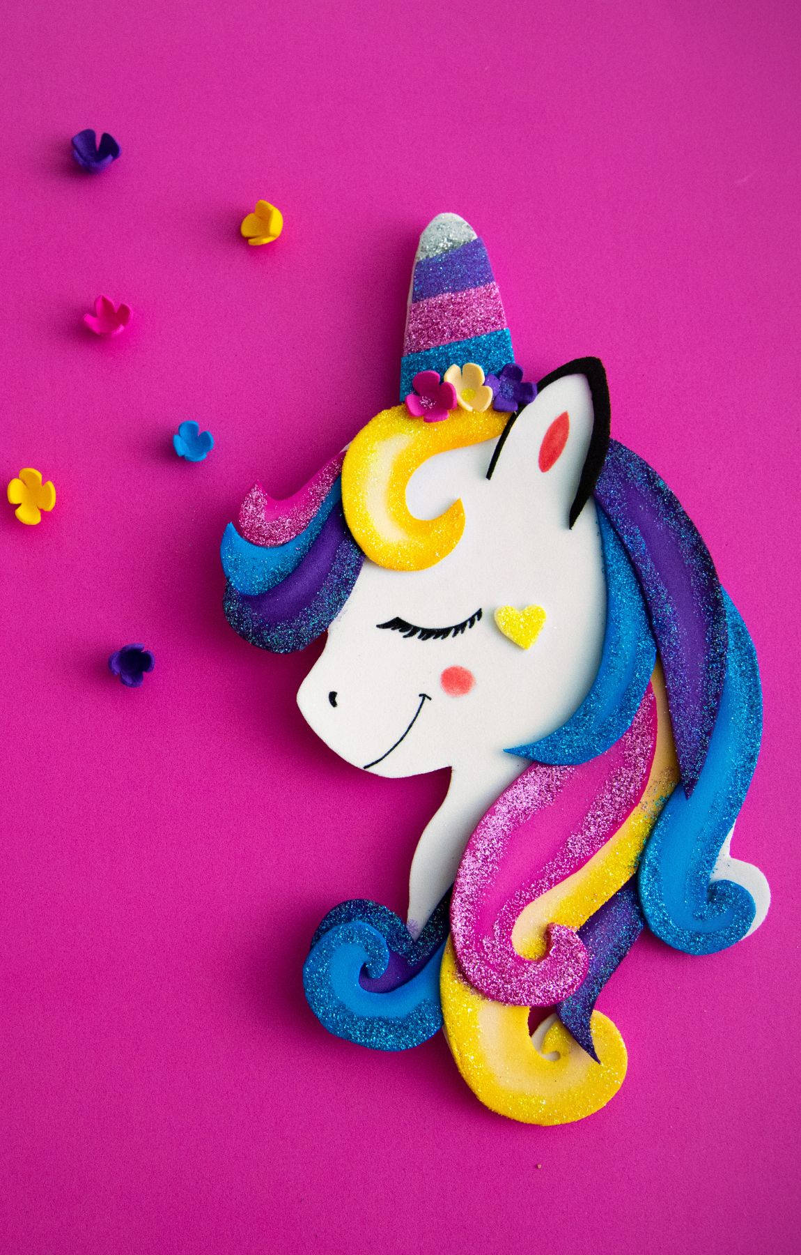 Cool Unicorn 桌布 壁紙 — 一個閃閃發光的彩虹獨角獸頭部手工藝品，閉著眼睛，面帶微笑，背景是鮮豔的粉紅色。
