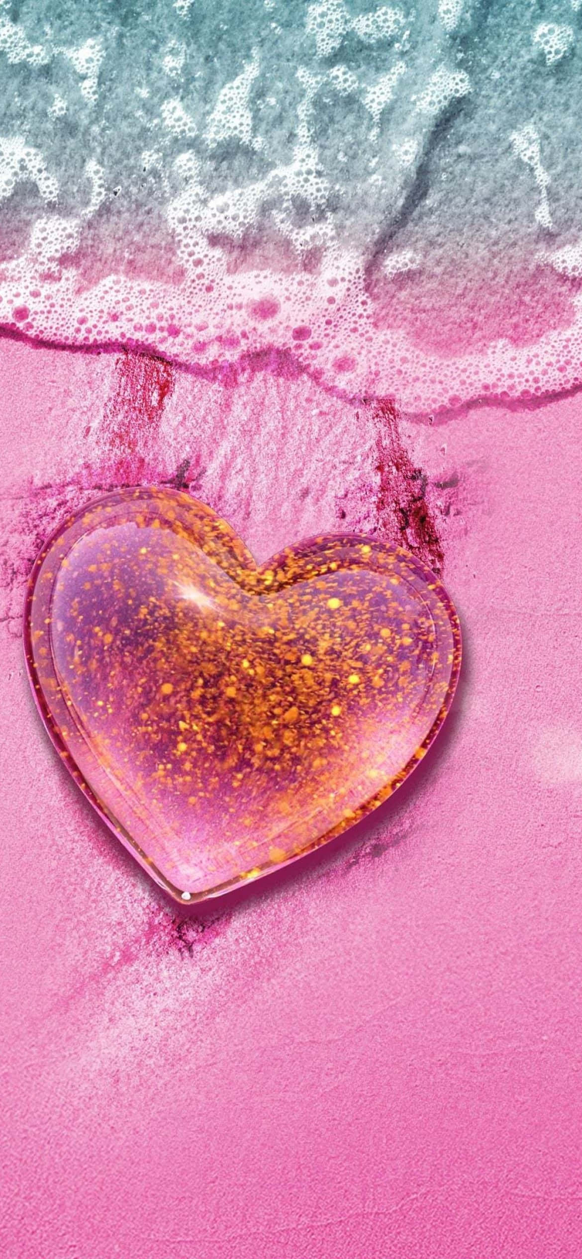 Beach Love 桌布 壁紙 — 一個閃閃發光的心形玻璃物體放在粉紅色的沙子上，綠松石色的海浪帶著白色泡沫輕輕拍打著它。