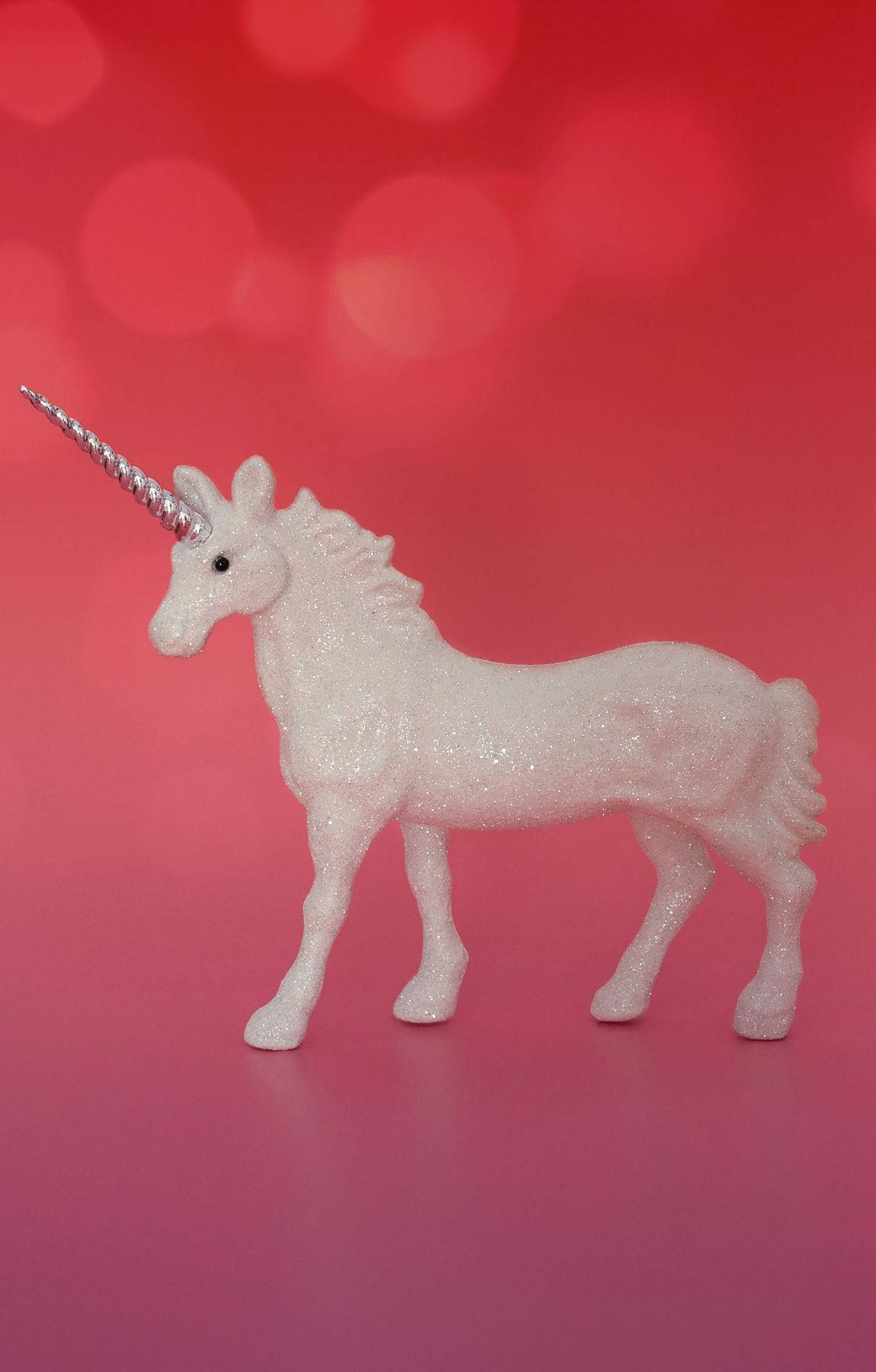 Cool Unicorn 桌布 壁紙 — 一個閃閃發光的白色獨角獸雕像，帶有銀色角，站在充滿活力的粉紅色散景背景前。