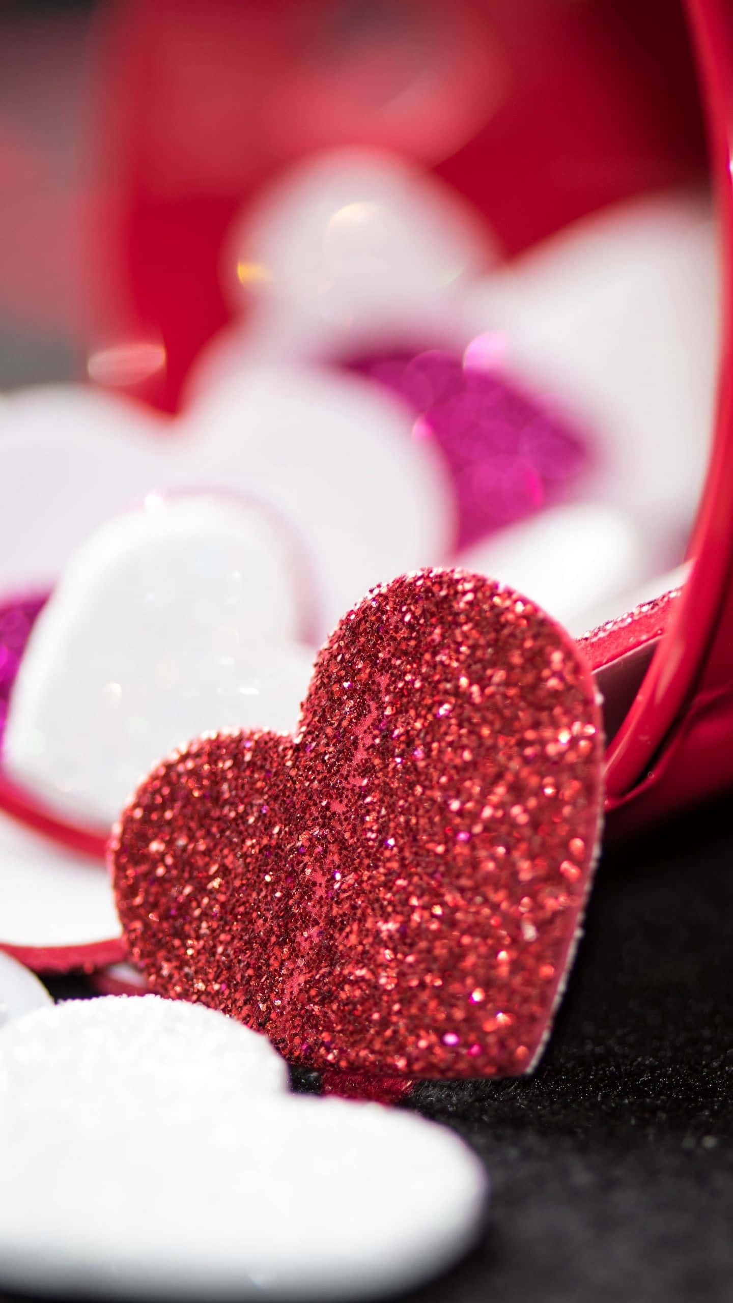 Glitter Pink Hearts 桌布 壁紙 — 一個閃閃發光的紅色亮粉愛心在從紅色容器中溢出的散落白色愛心中成為焦點。