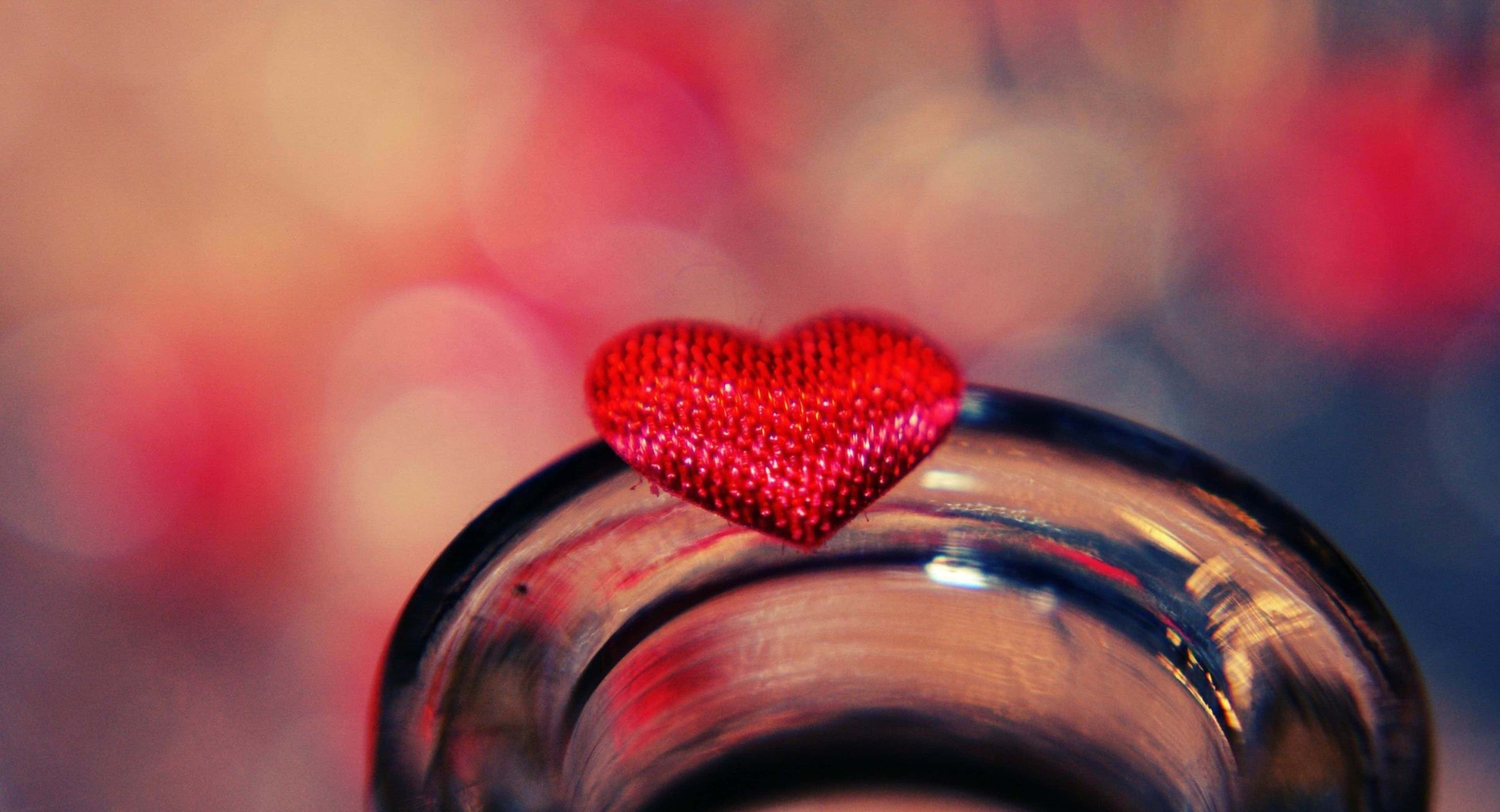 Sweet Love 桌布 壁紙 — 一個閃閃發光的紅色心形裝飾品放在玻璃瓶上，背景是柔和模糊的暖紅色和粉紅色。