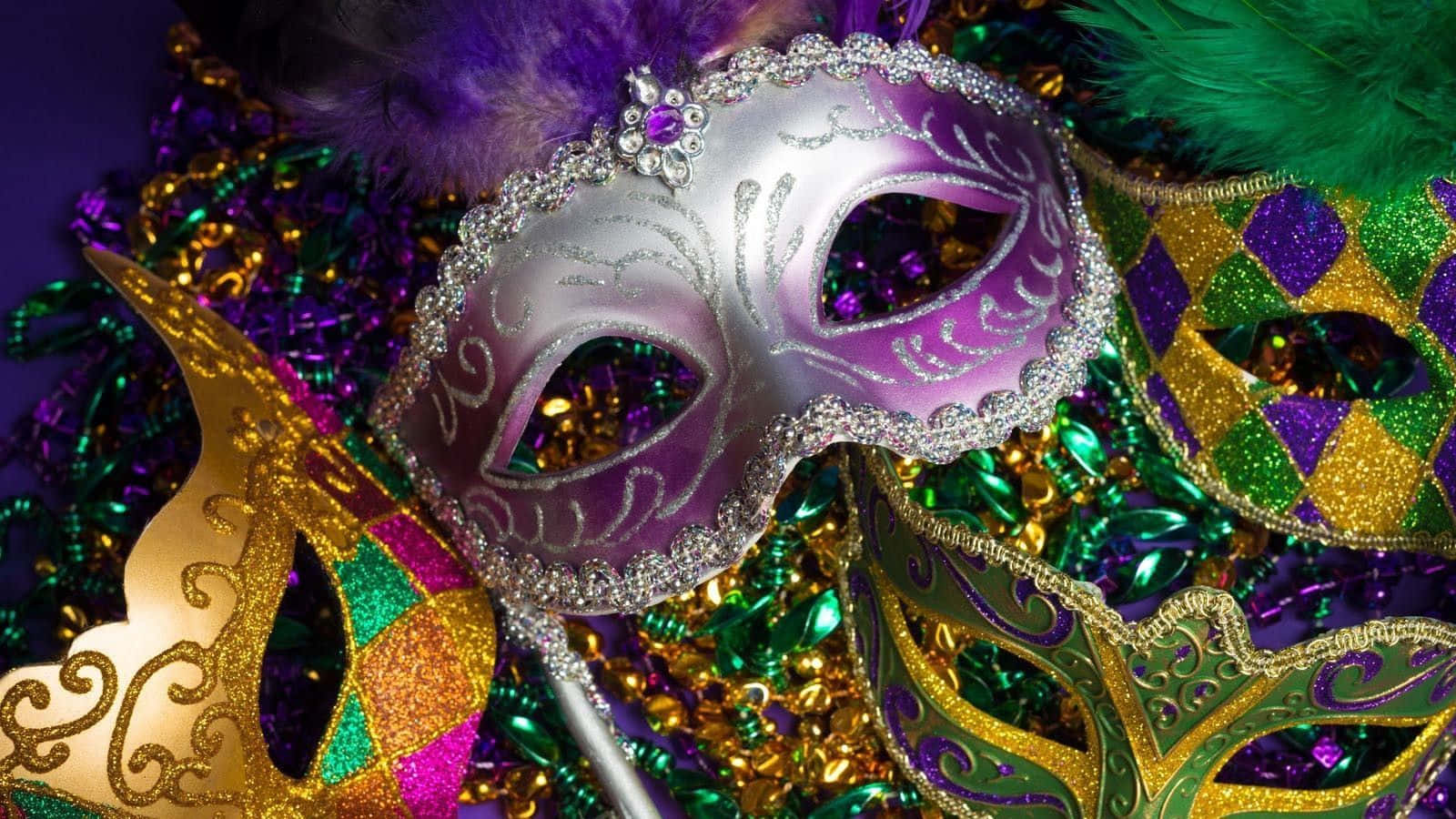 Mardi Gras 桌布 壁紙 — 一個閃閃發光的紫色和銀色威尼斯面具，飾有羽毛，放在一堆充滿活力的狂歡節珠子和亮片上。