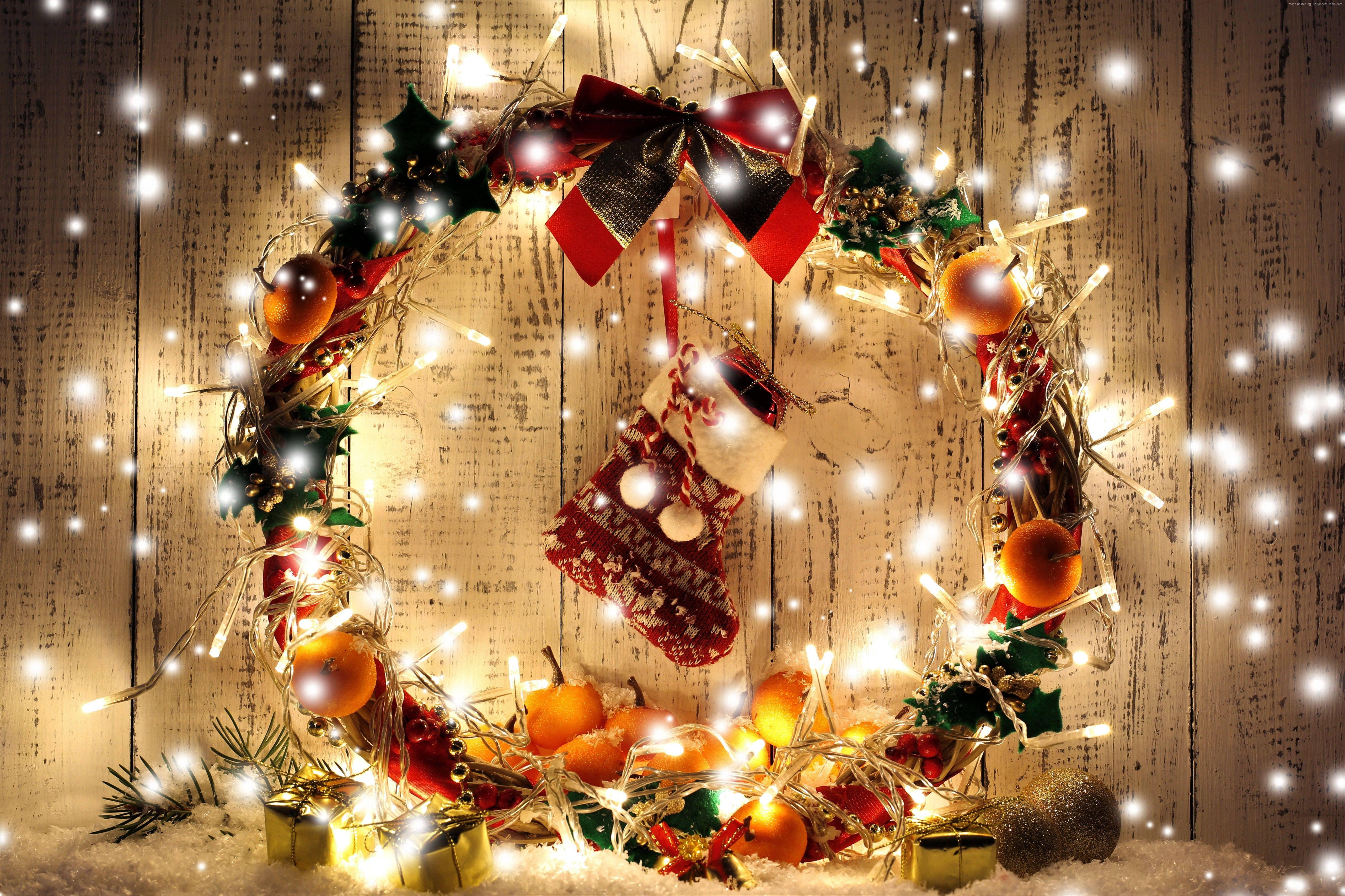 Wreath 桌布 壁紙 — 一個閃閃發光的聖誕花環，飾有燈飾、裝飾品和紅色蝴蝶結，掛在灑滿白雪的質樸木牆上。