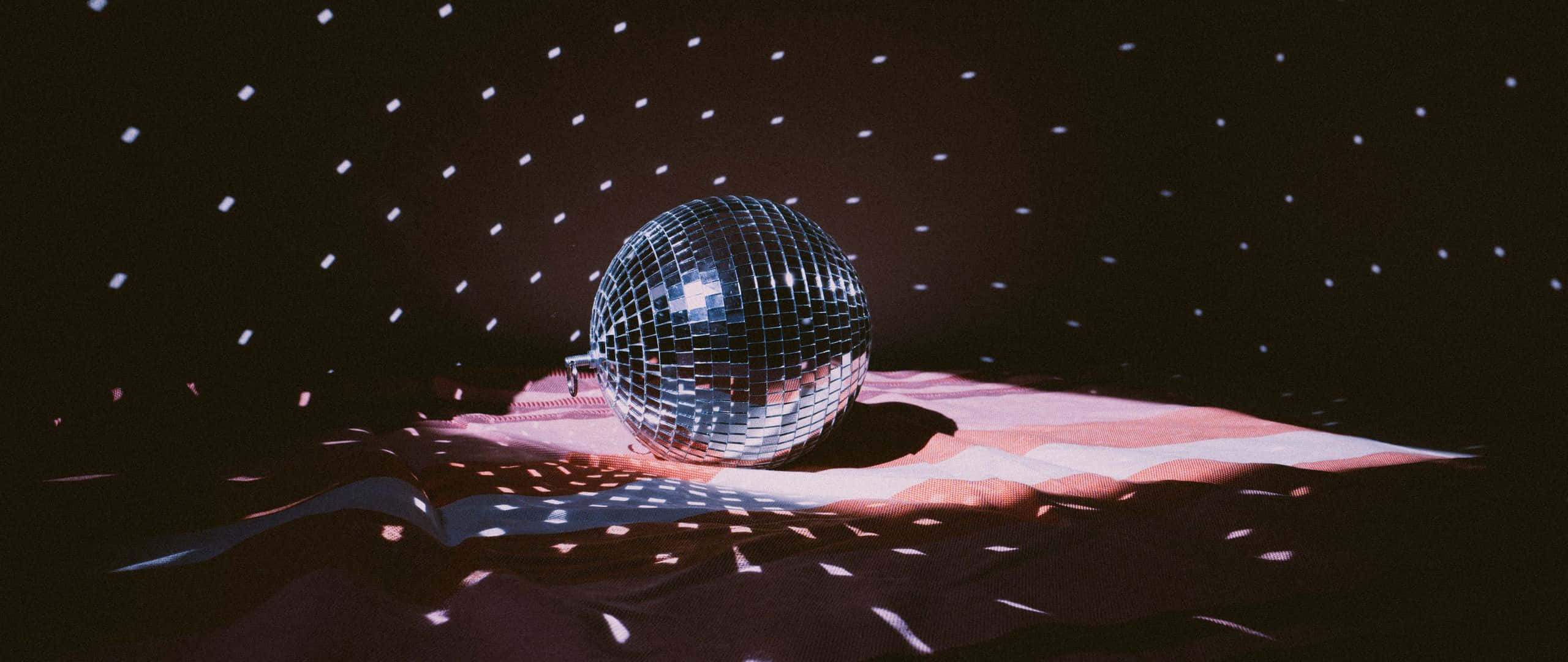 disco ball 桌布 壁紙 — 一個閃閃發光的迪斯可球放在粉紅色布料上，背景是繁星點點的夜空，散落著五彩紙屑。