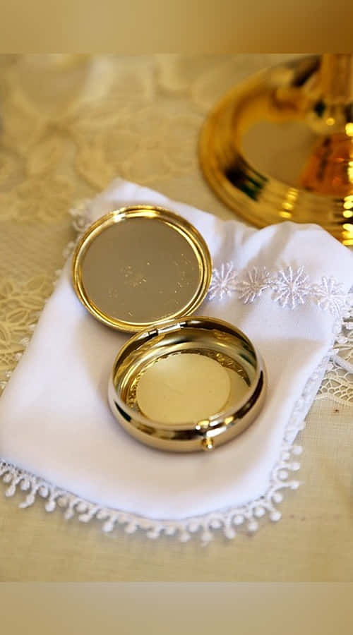 Sacrament 桌布 壁紙 — 一個閃閃發光的金色粉盒鏡子打開著，放在一塊白色蕾絲邊布上，旁邊有一個金色燭台。
