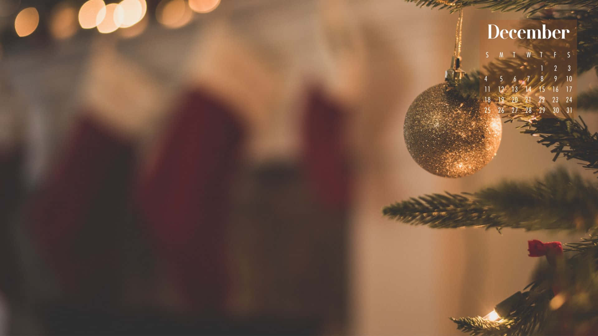 Cute December 桌布 壁紙 — 一個閃閃發光的金色聖誕裝飾掛在松樹枝上，帶有十二月日曆疊加層和背景中溫暖的散景燈光。