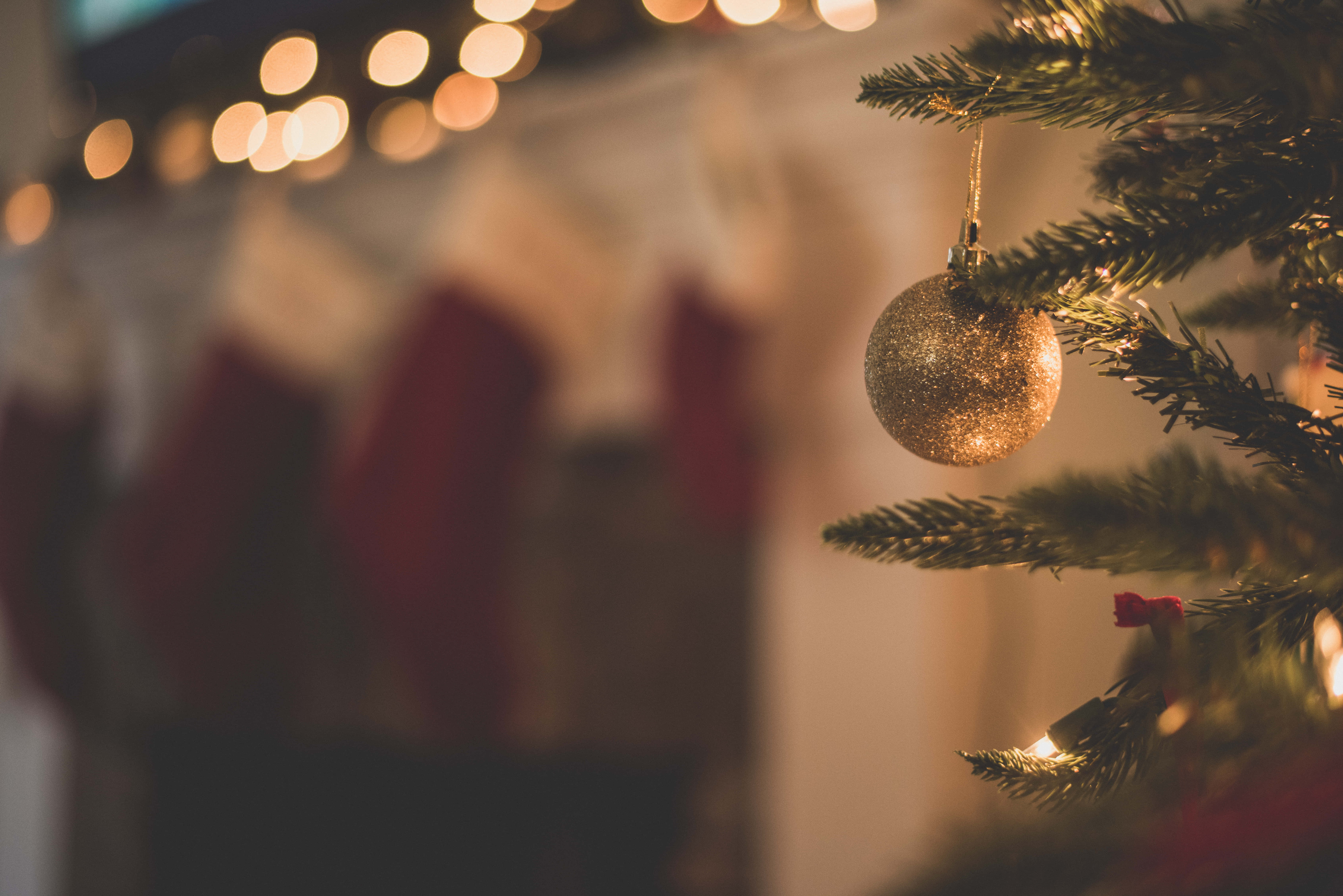Winter Christmas Desktop 桌布 壁紙 — 一個閃閃發光的金色裝飾品掛在松樹枝上的特寫，背景有溫暖的散景燈光和紅色聖誕襪。