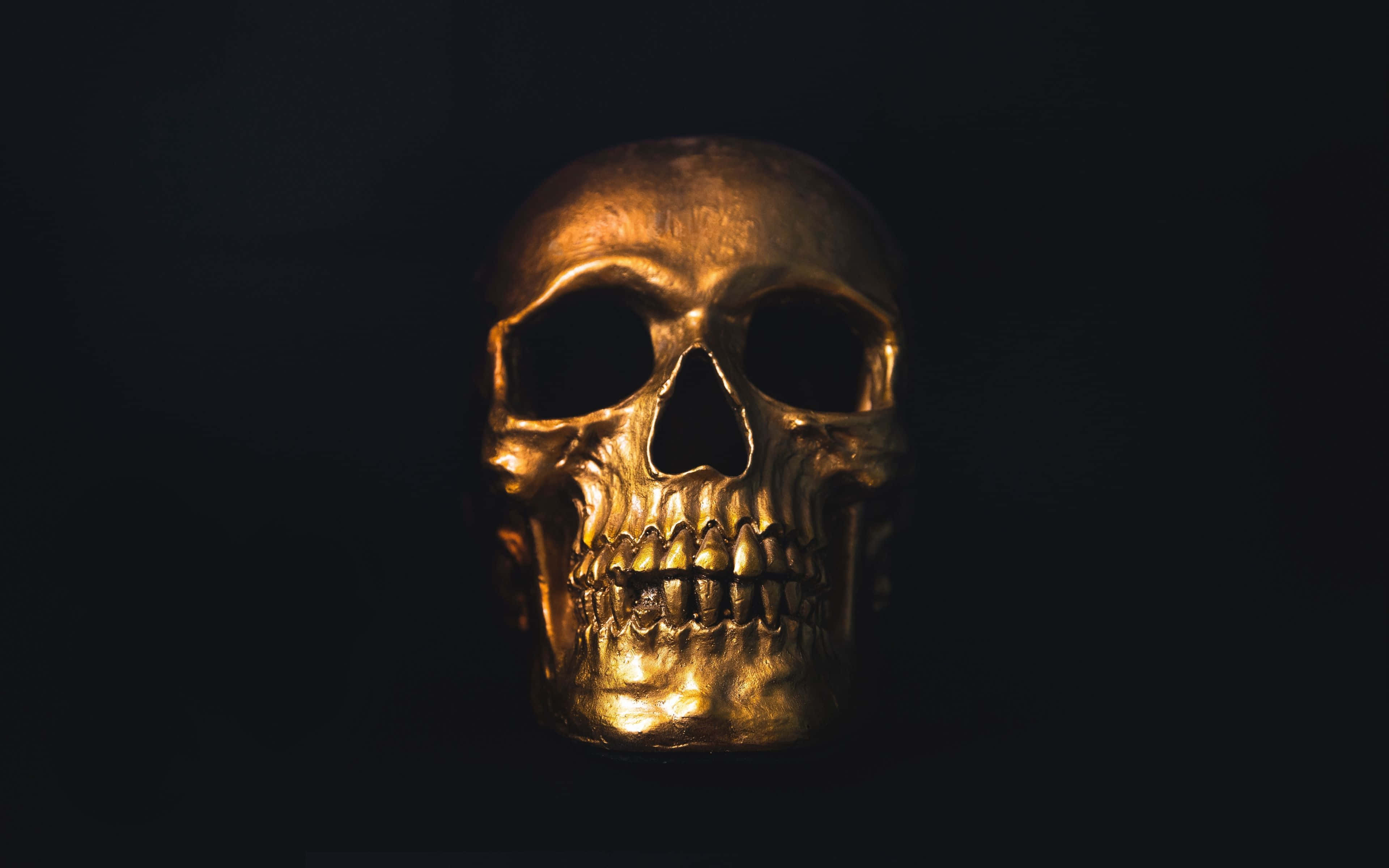 Awesome Skull 桌布 壁紙 — 一個閃閃發光的金色頭骨，在漆黑背景上以戲劇性燈光照亮。