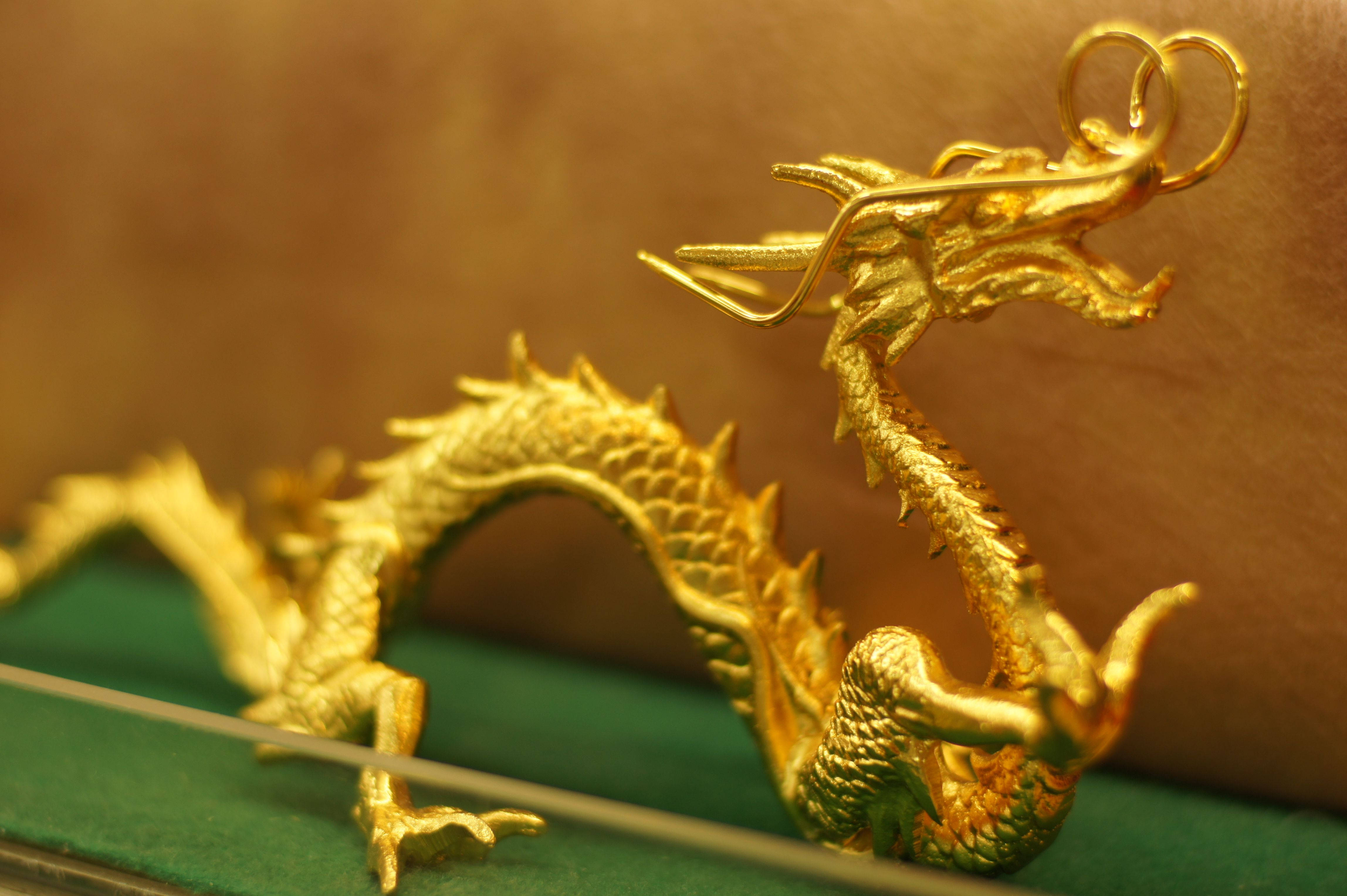 Gold Dragon 桌布 壁紙 — 一個閃閃發光的金色龍雕像，帶有複雜的鱗片和舉起的爪子，放在綠色天鵝絨表面上。
