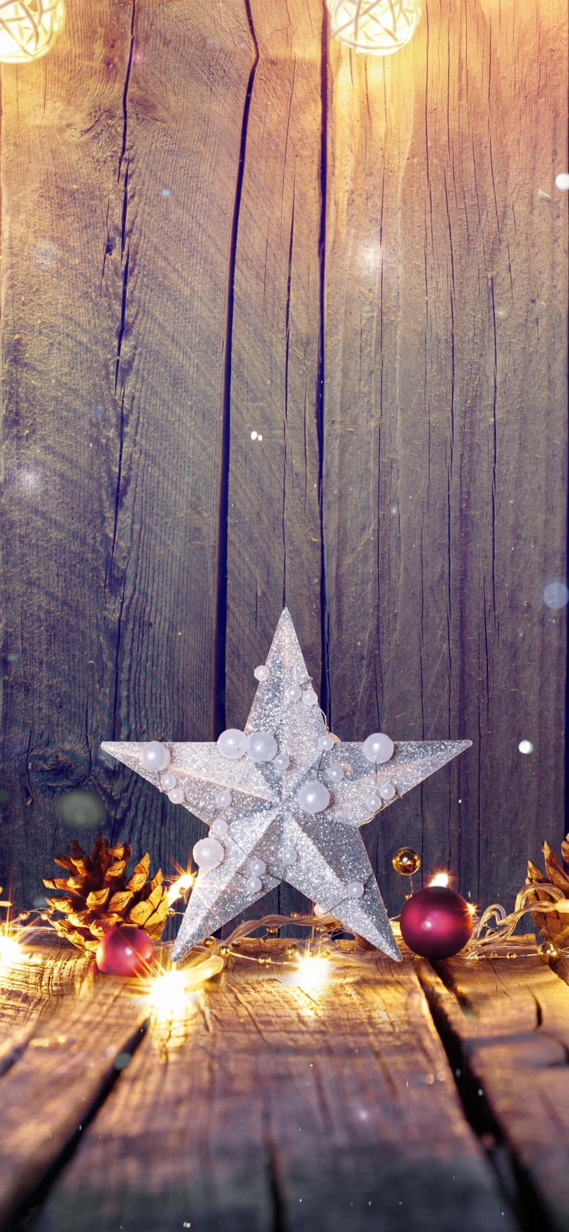 Christmas Star 桌布 壁紙 — 一個閃閃發光的銀色星星裝飾品放在質樸的木板上，周圍環繞著松果和溫暖的仙女燈。