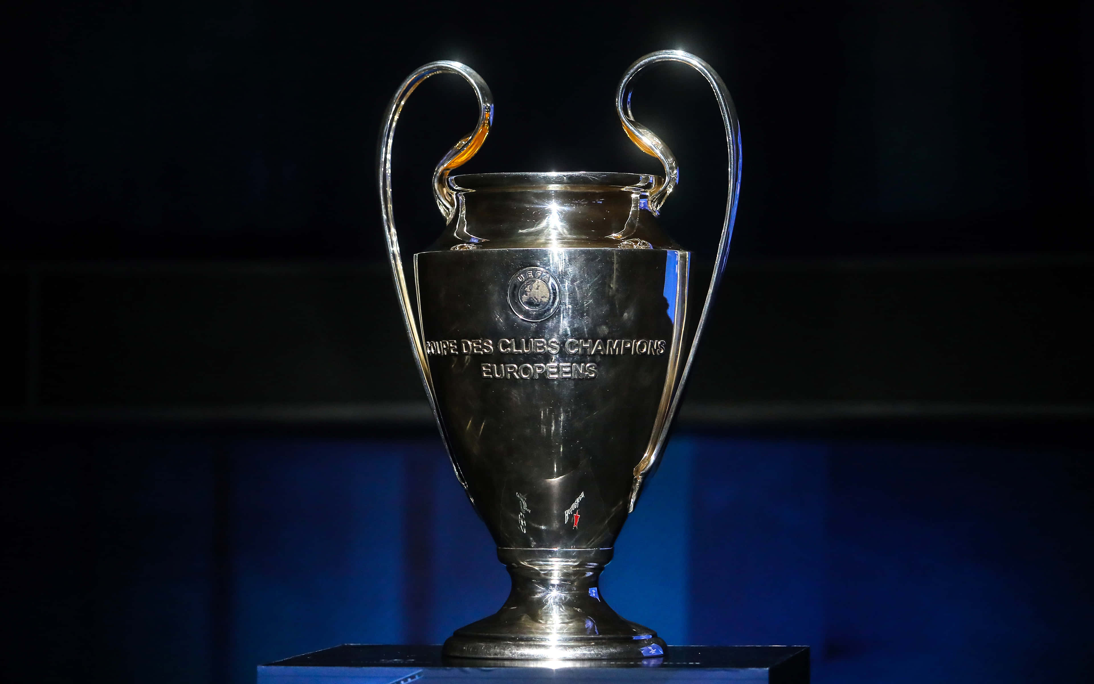 Champions League 桌布 壁紙 — 一個閃閃發光的銀色歐洲冠軍聯賽獎盃，在深藍色背景的聚光燈照射下。