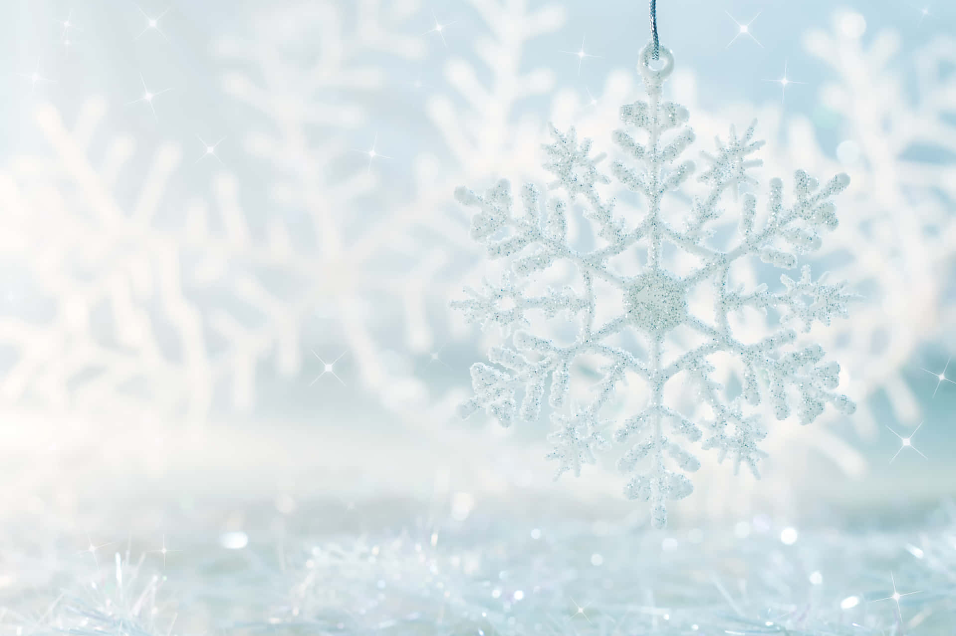 Festive 桌布 壁紙 — 一個閃閃發光的銀色雪花裝飾品懸掛在柔和模糊的冬季背景中，帶有閃爍的光效。