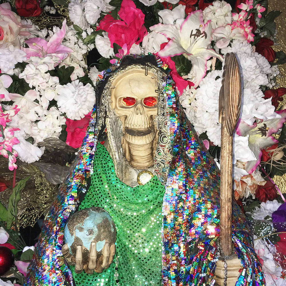 Santa Muerte 桌布 壁紙 — 一個閃閃發光的骷髏人物，披著亮片長袍，手持一個被鮮豔粉紅色和白色花朵包圍的地球儀。