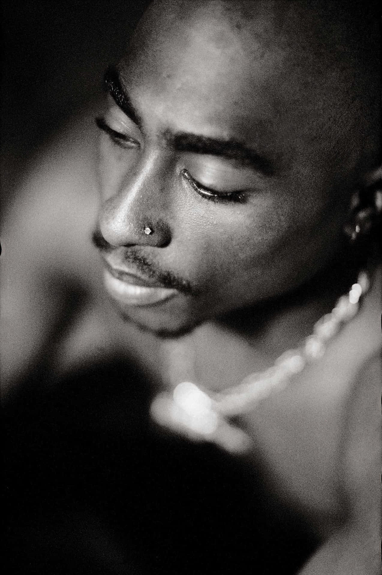 tupac 桌布 壁紙 — 一個閉上眼睛、戴鼻環的男士的黑白特寫肖像，在模糊的深色背景下柔和打光。