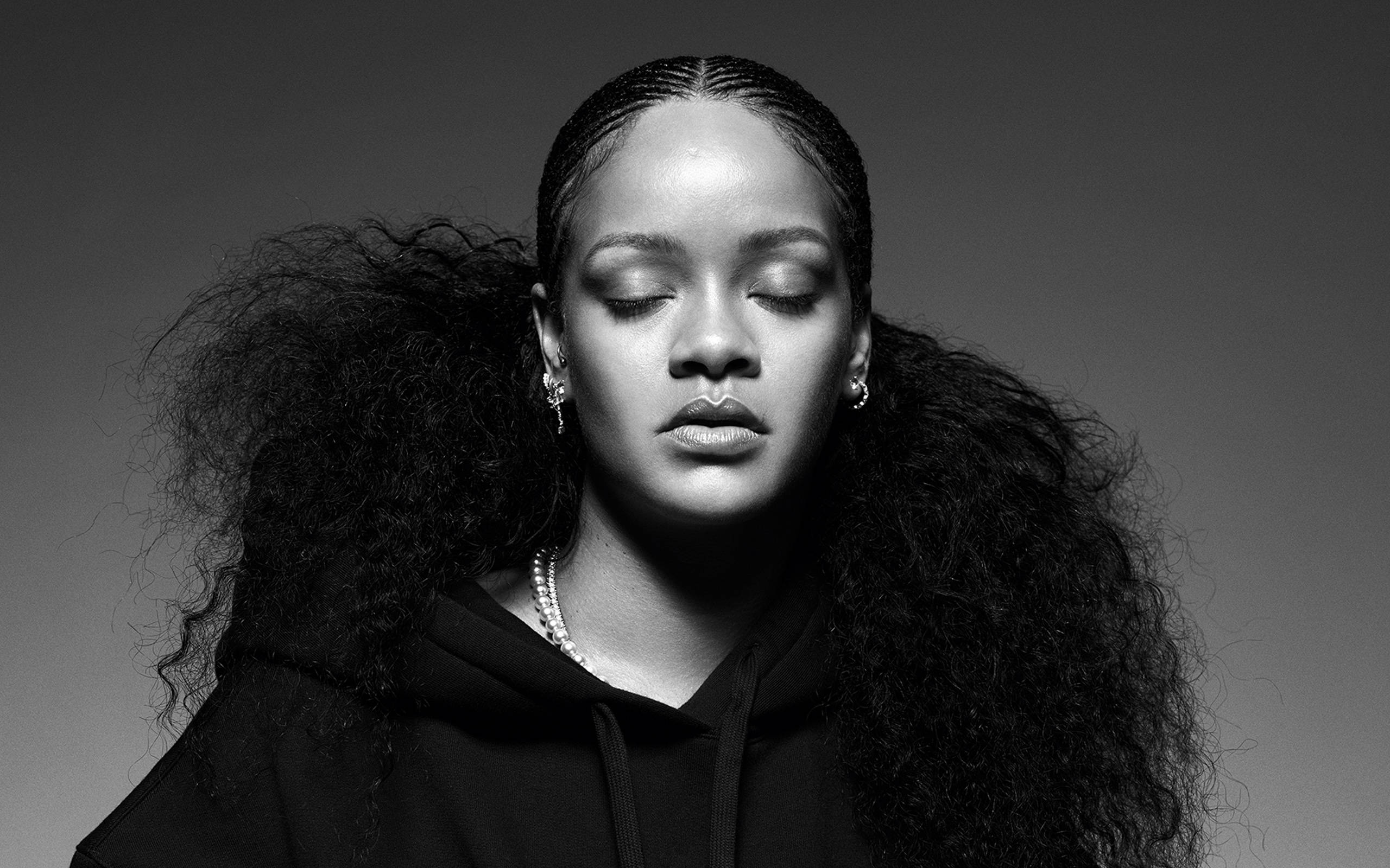 Rihanna 桌布 壁紙 — 一個閉上眼睛、擁有豐盈捲髮的女性黑白肖像，穿著連帽衫和珍珠項鍊。