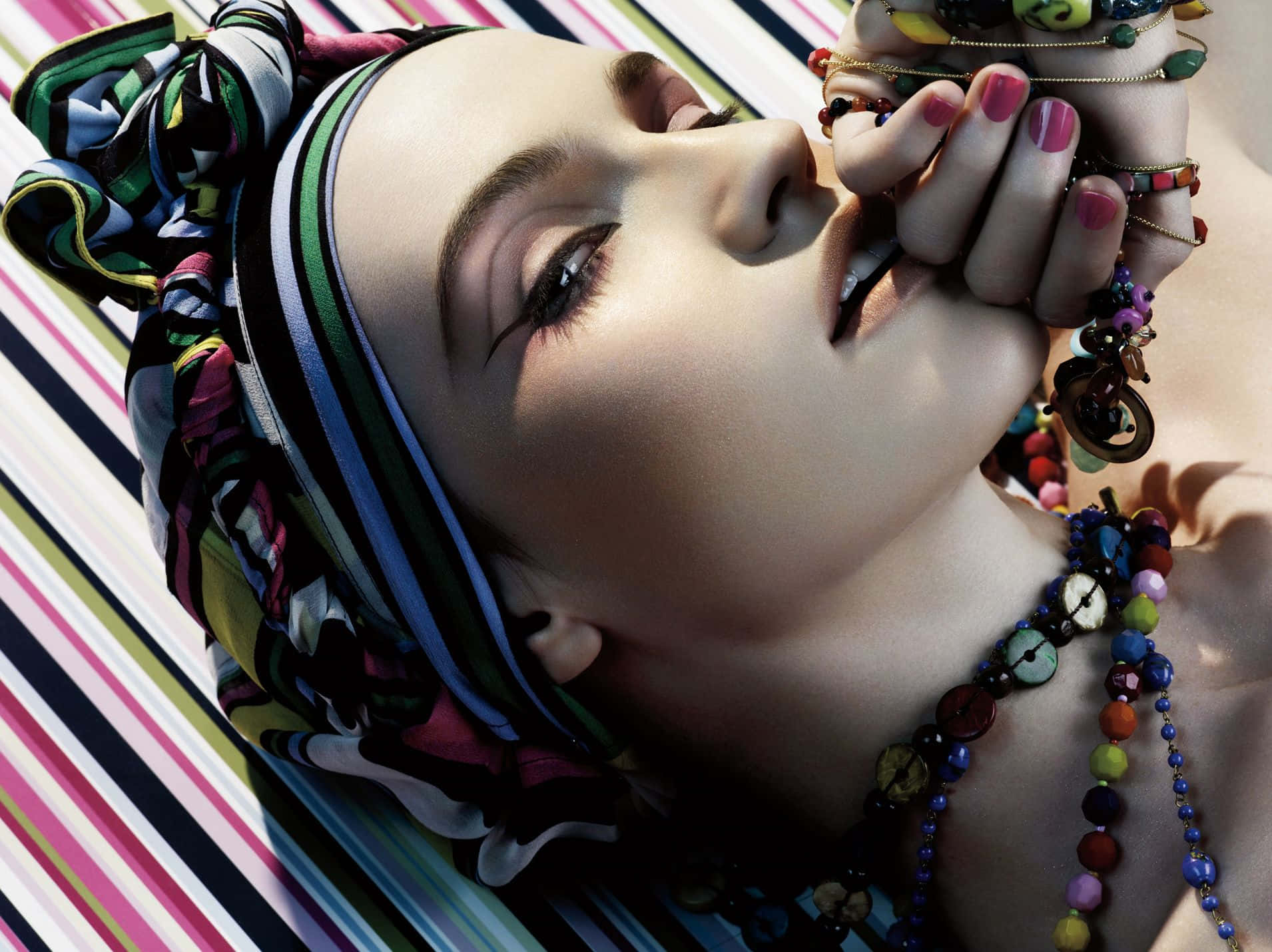 Mac Cosmetics 桌布 壁紙 — 一個閉上眼睛的女人將頭靠在條紋背景上，裝飾著彩色珠子和圖案頭巾。