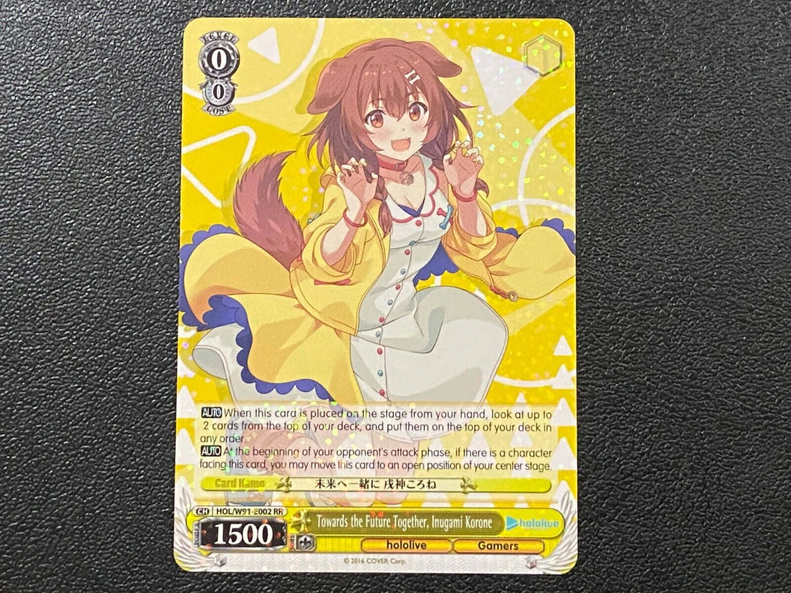 Inugami Korone 桌布 壁紙 — 一個開心的動漫女孩，棕色頭髮，黃色外套，在深色紋理背景的收藏卡上燦爛微笑。
