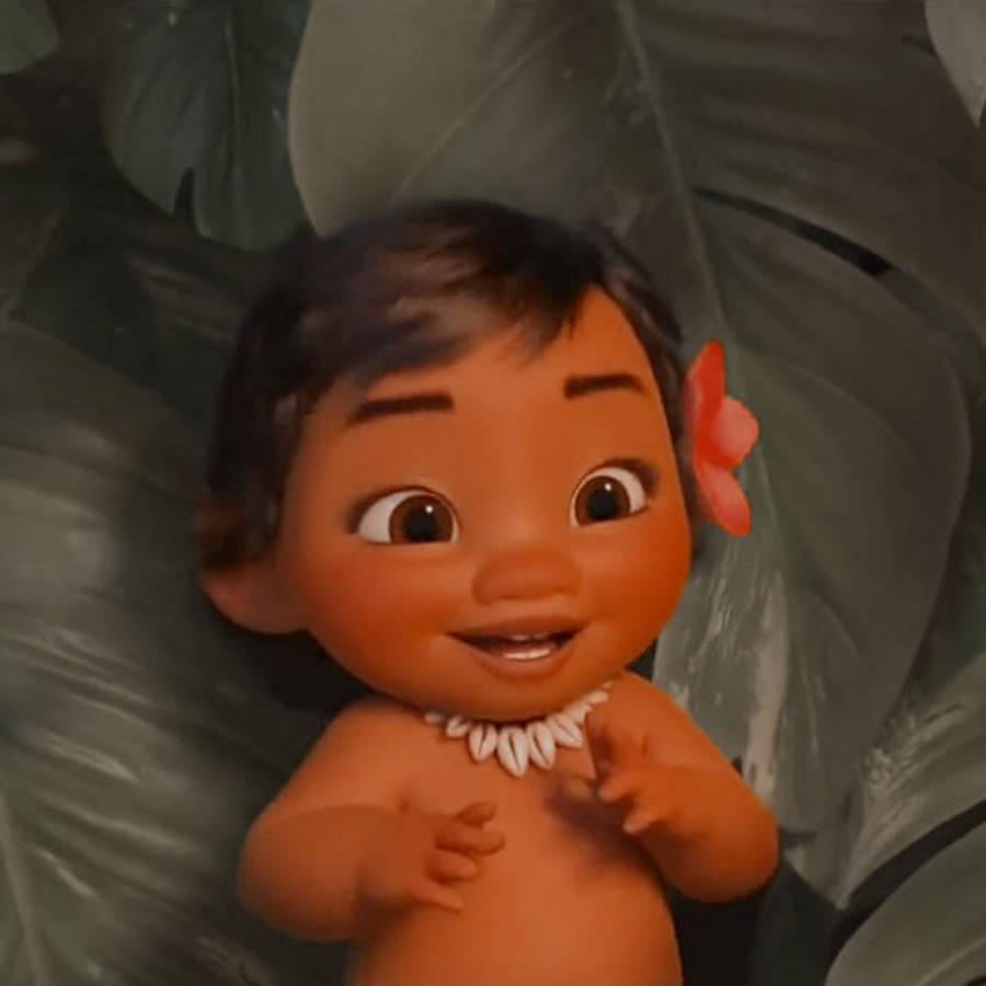 Baby Moana 桌布 壁紙 — 一個開心的動畫寶寶，深色頭髮，耳後插著一朵粉紅花，依偎在大綠葉中微笑。