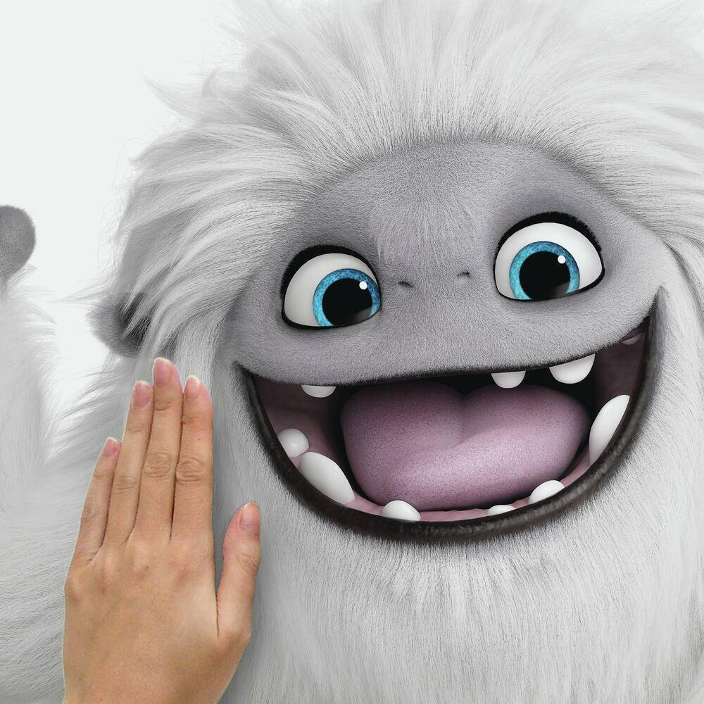 電影動圖 桌布 壁紙 — 一個開心的動畫雪怪，有明亮的藍眼睛和露出牙齒的寬闊笑容，有一隻人類的手輕輕觸摸它的臉頰。